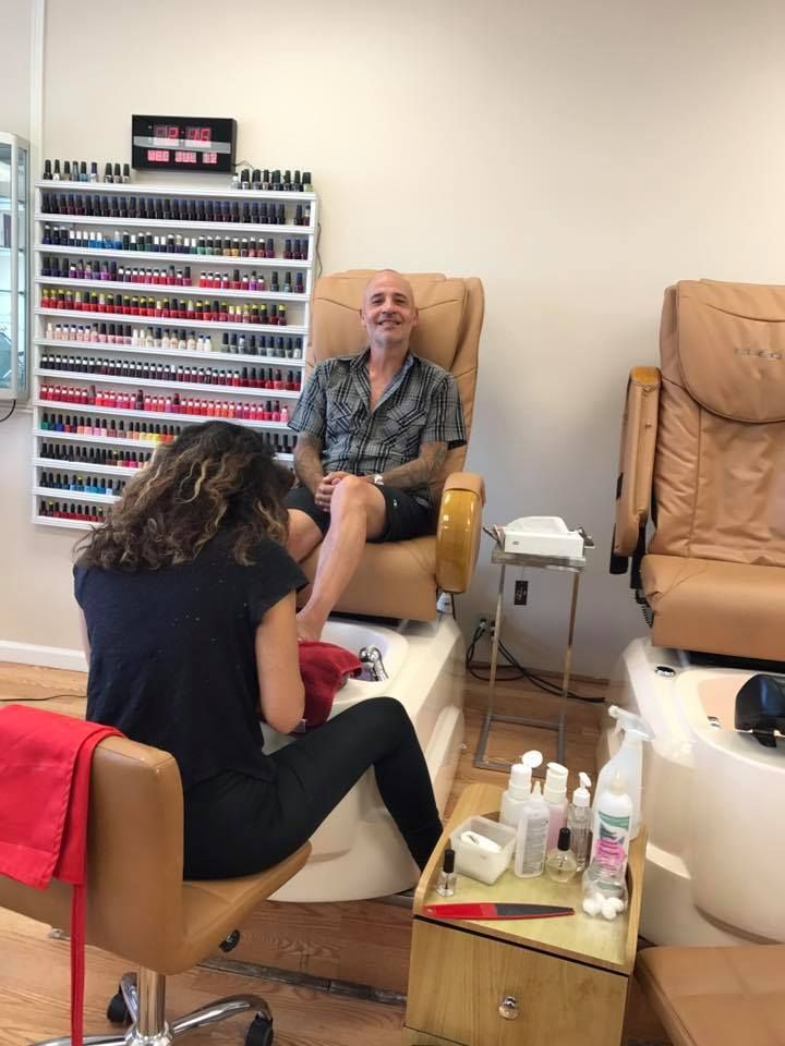 A man is sitting in a chair getting his nails done by a woman in a nail salon.