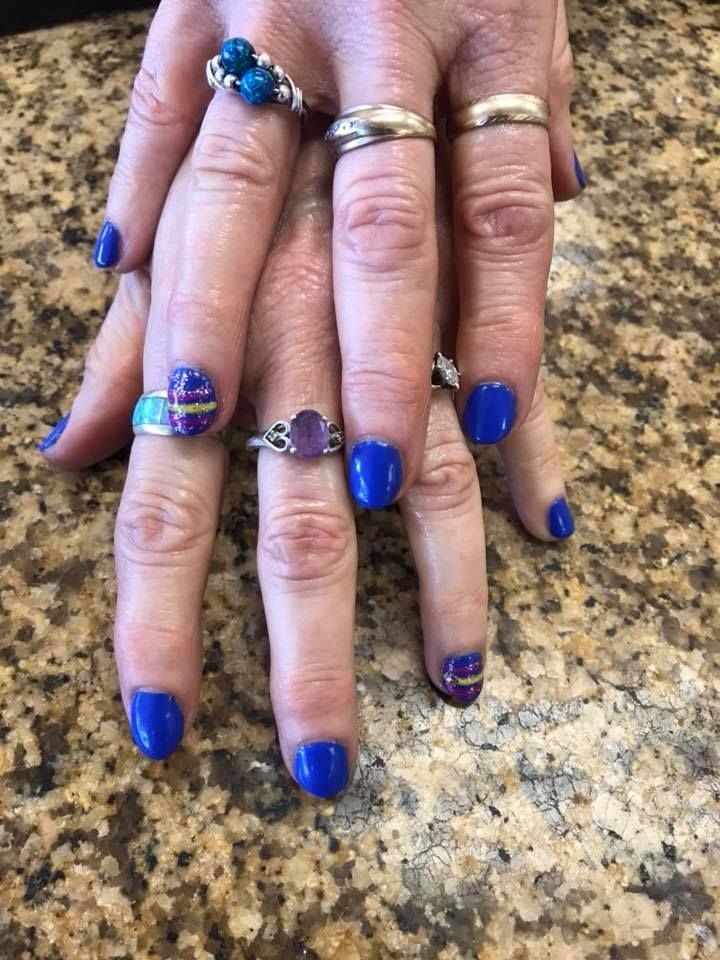 A woman 's hands with blue nails and rings on them.