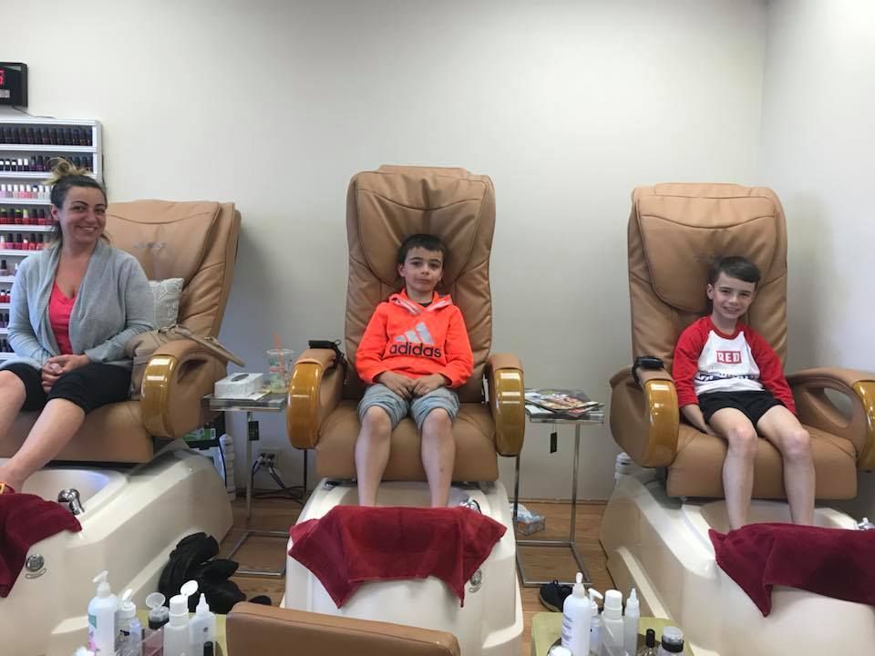 A woman and two children are sitting in chairs at a nail salon.
