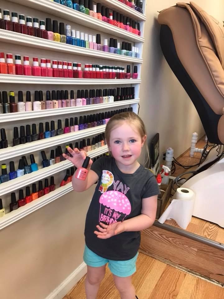 A little girl is standing in front of a wall of nail polish.