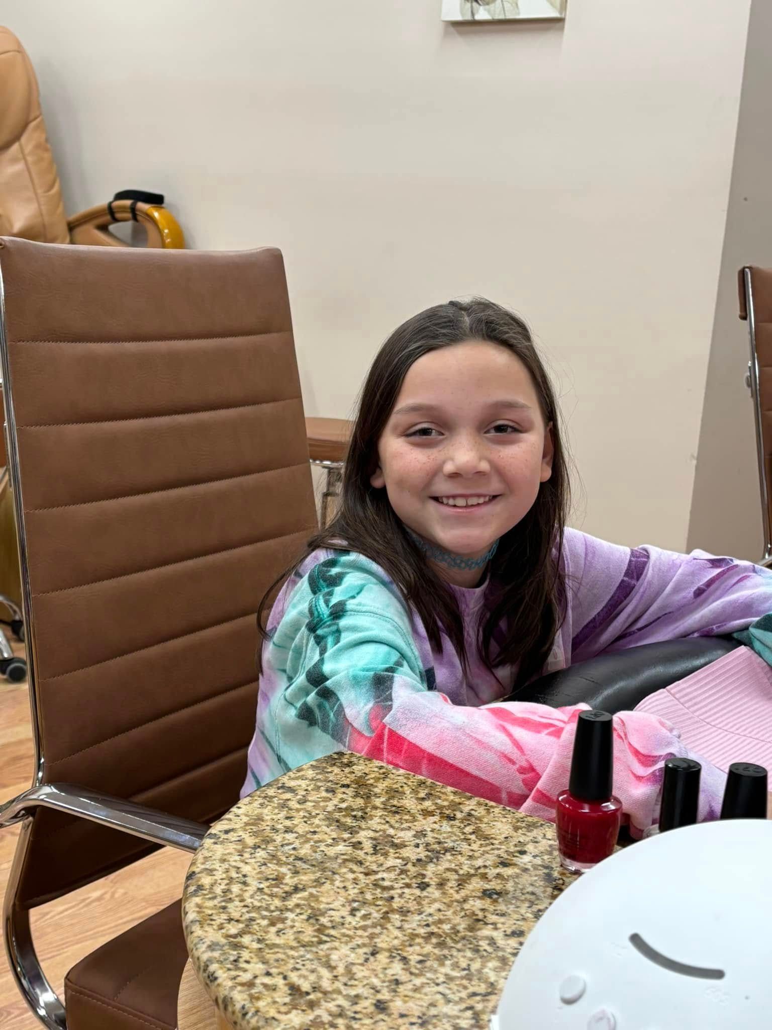 A young girl is sitting at a table with bottles of nail polish.