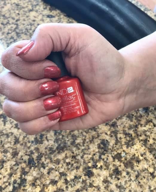 A woman is holding a bottle of red nail polish