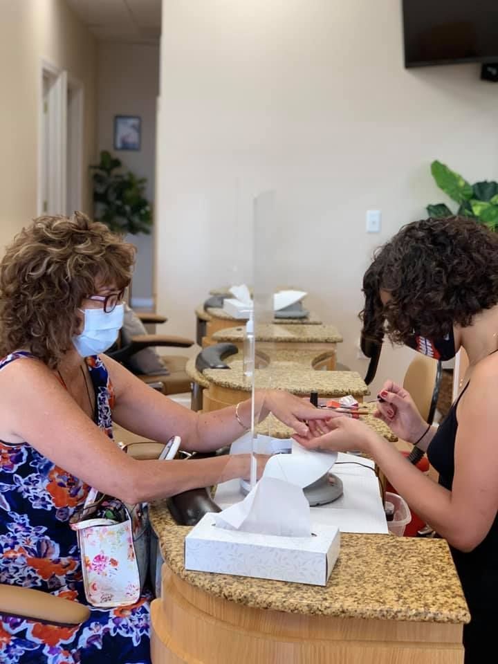 A woman is getting her nails done at a nail salon while wearing a mask.