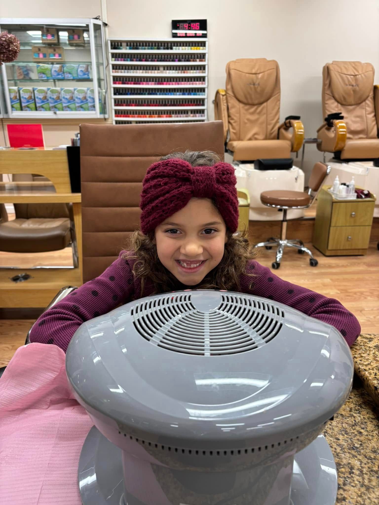 A little girl is sitting in a chair in a nail salon.