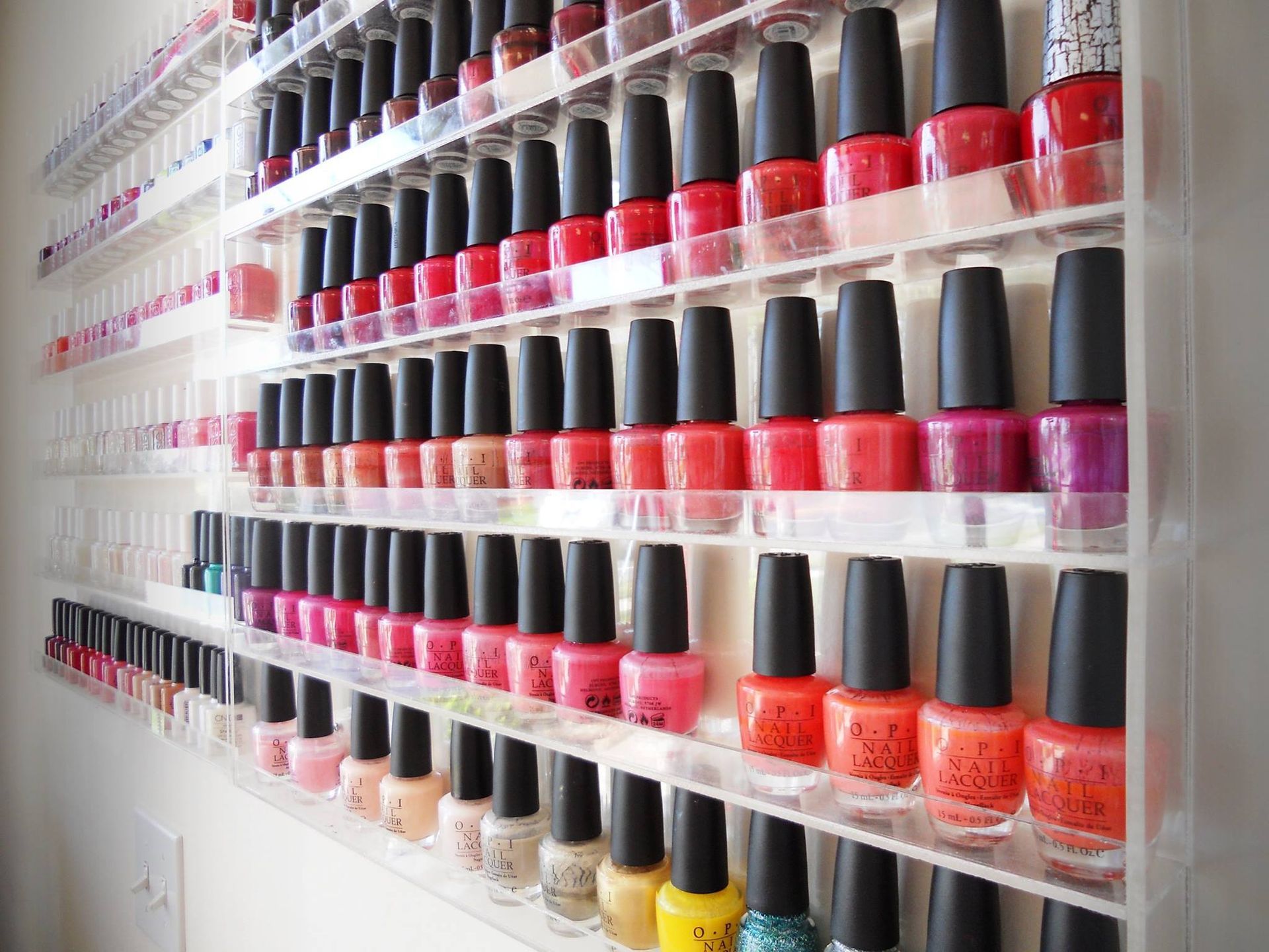Many bottles of nail polish are lined up on a shelf.