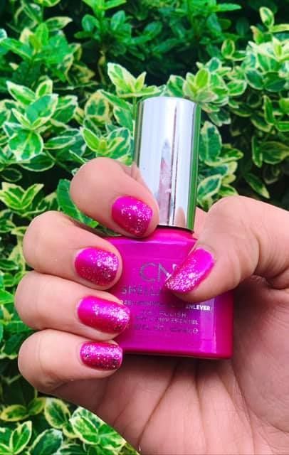 A person holding a bottle of pink nail polish in their hand.