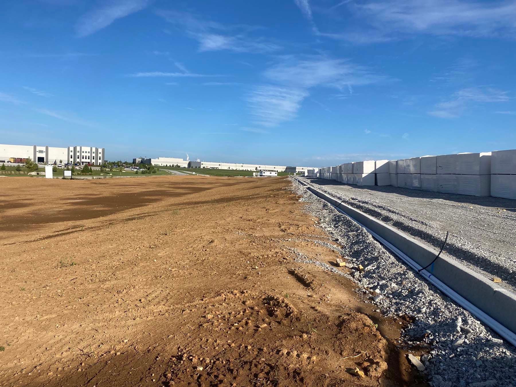 A large dirt field with a train track in the foreground and a building in the background.