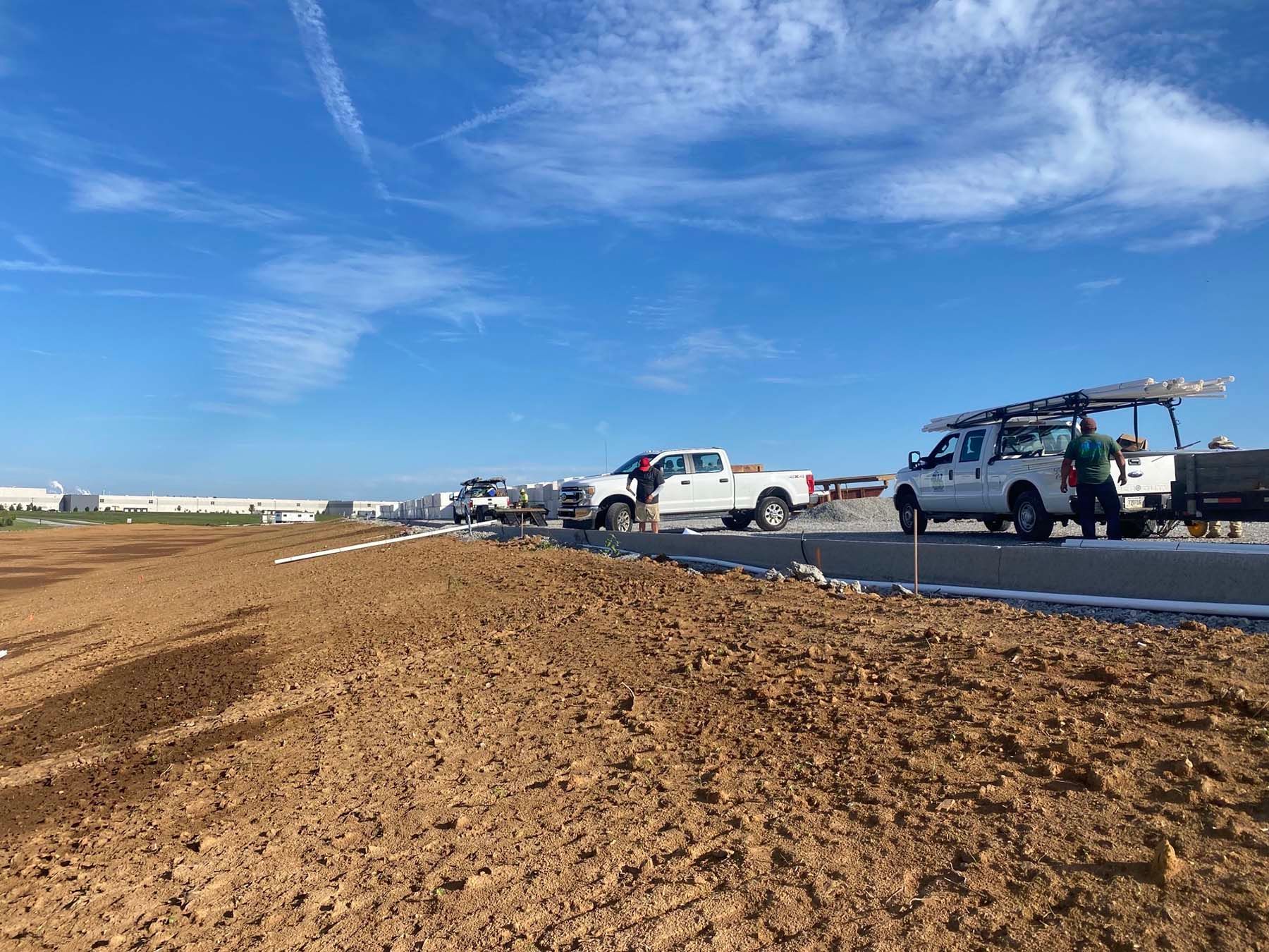 A group of construction trucks are parked on the side of a dirt road.