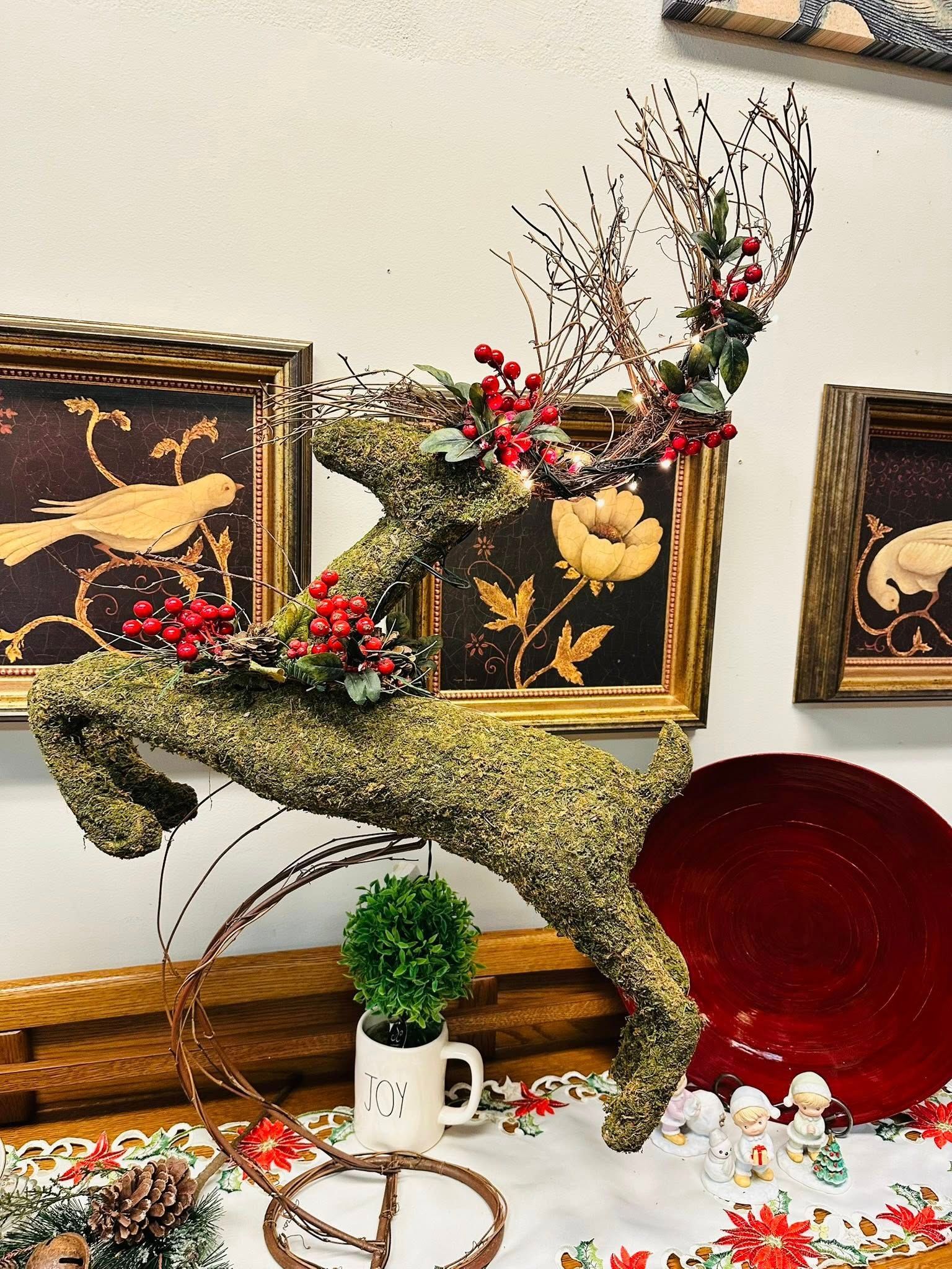 Christmas reindeer decoration covered in moss with red berries and a round red plate.