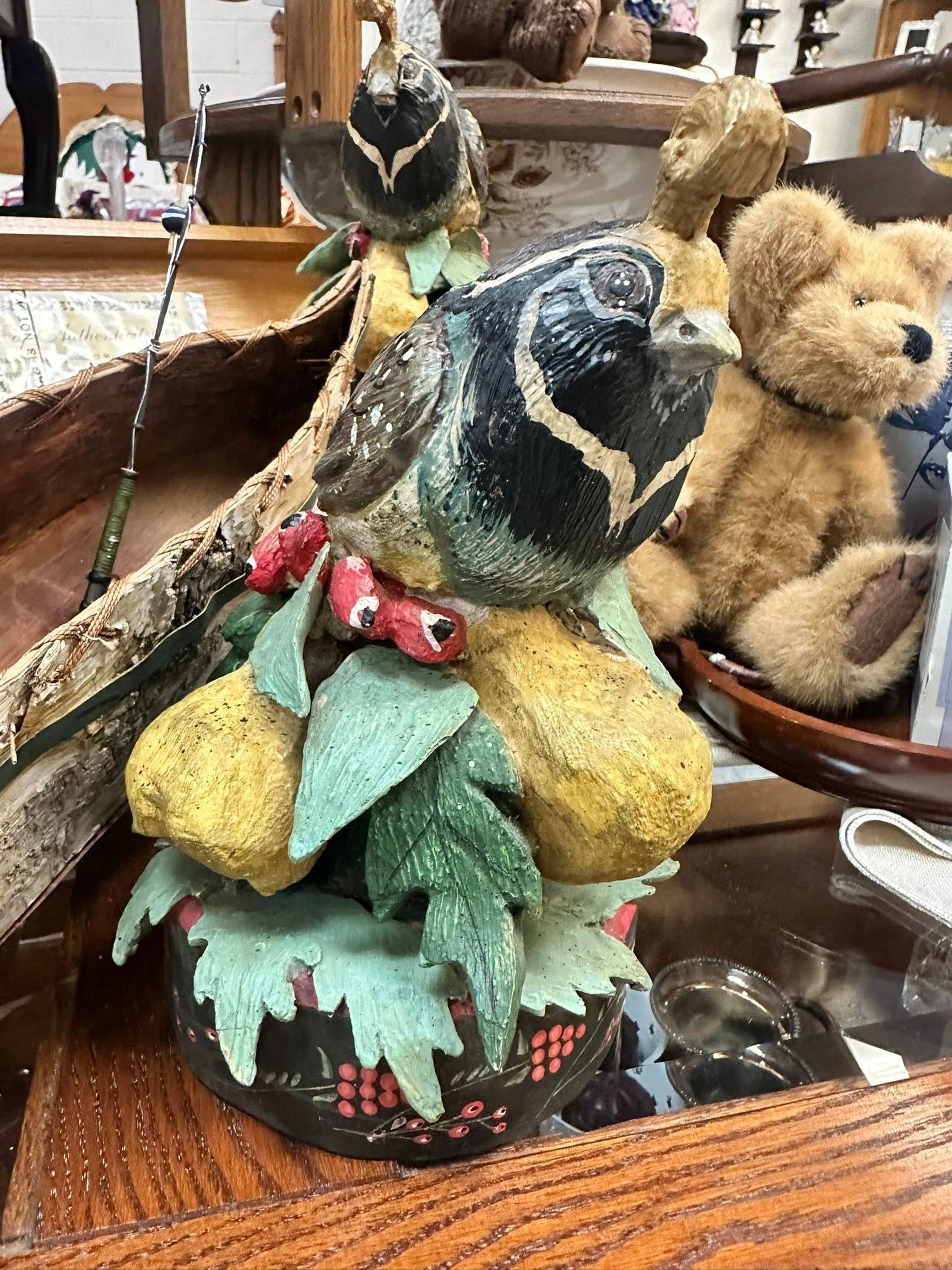 Statue of a bird with a black head and tan body, perched on a decorative base with green leaves and red berries.