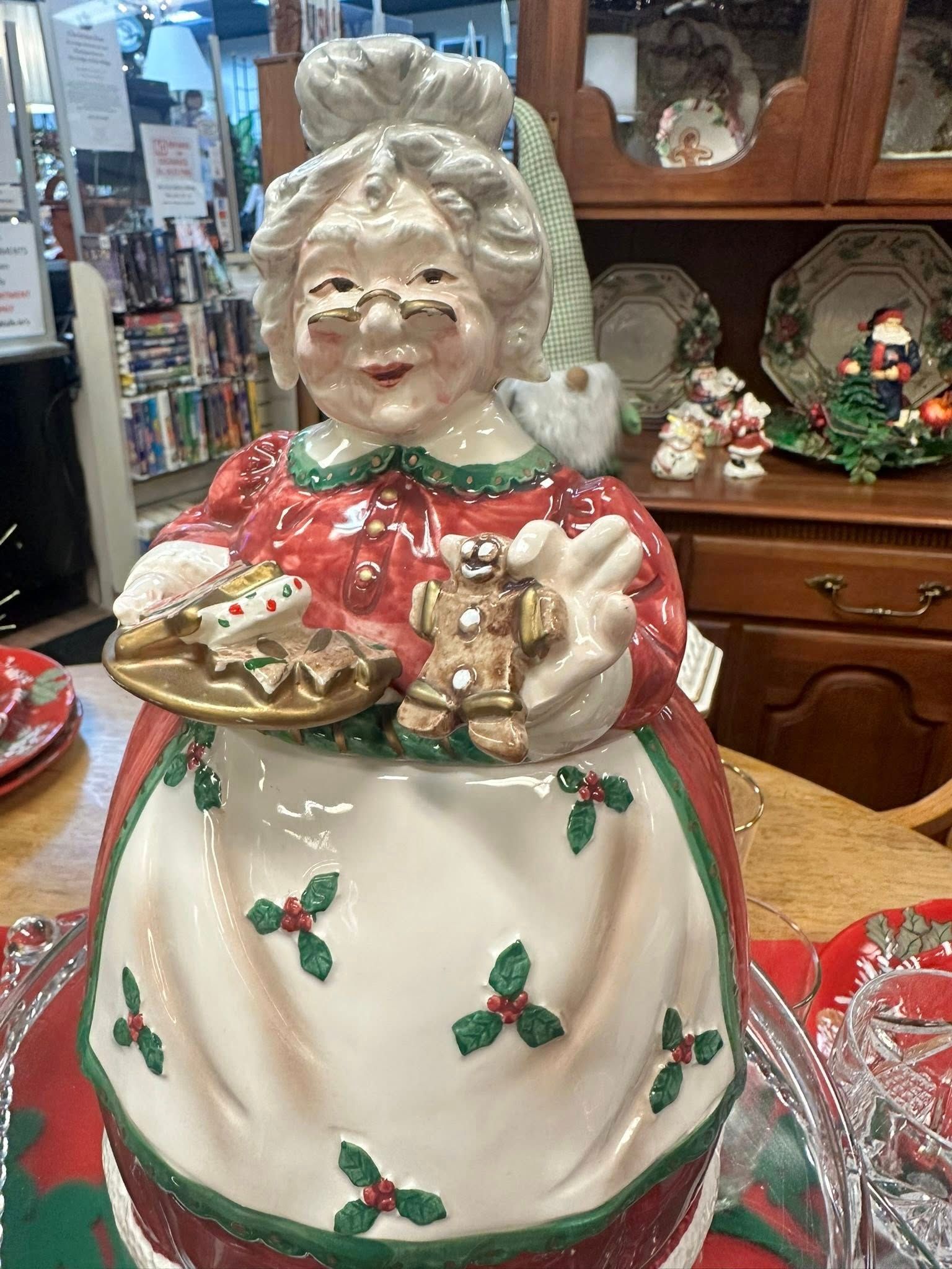 Mrs. Claus ceramic cookie jar holding gingerbread and cookies, red dress, holly apron, and smiling face.