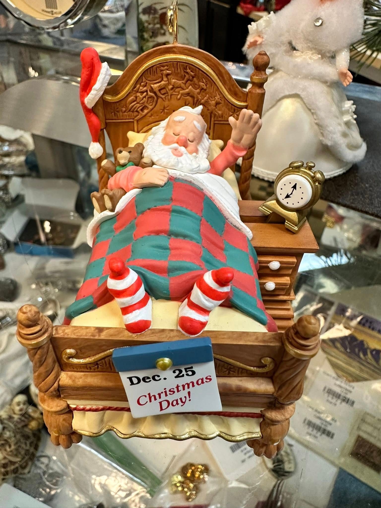 Santa Claus figurine in bed, waving; Christmas Day is on the calendar.