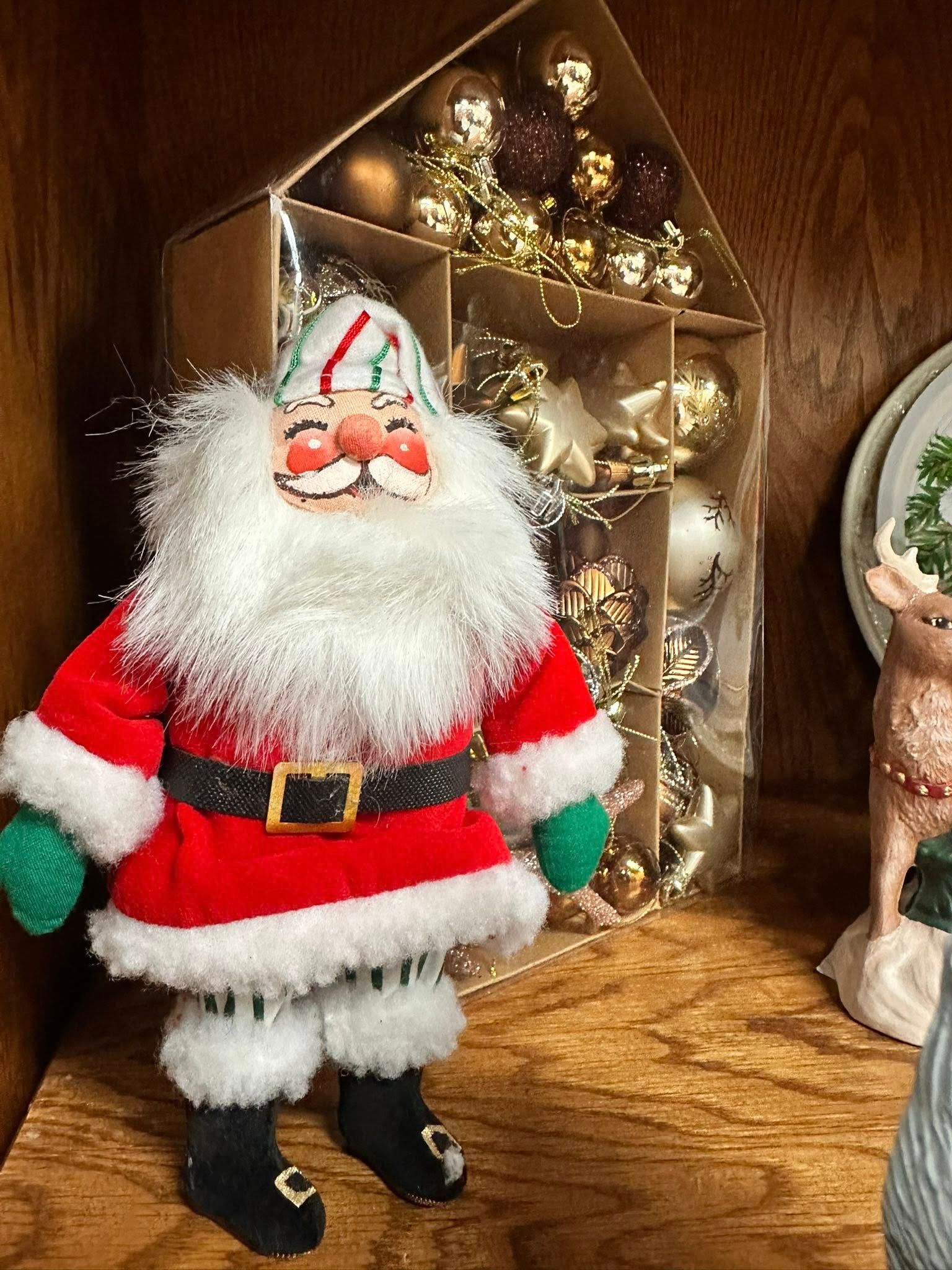 Santa Claus figurine on a shelf with a house-shaped ornament holder filled with gold ornaments.