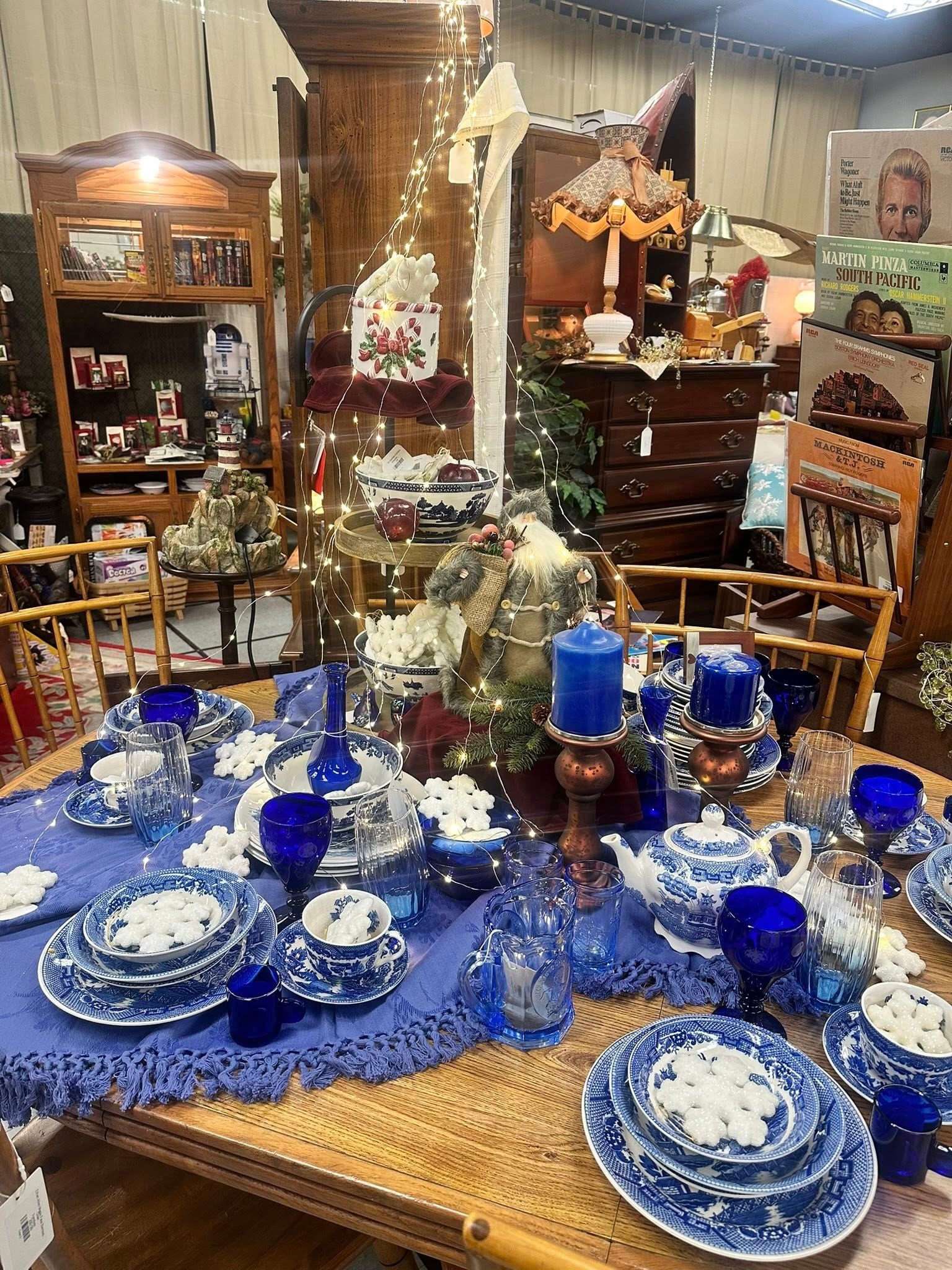 A table set with blue and white china, candles, and decorations in a room filled with antiques.