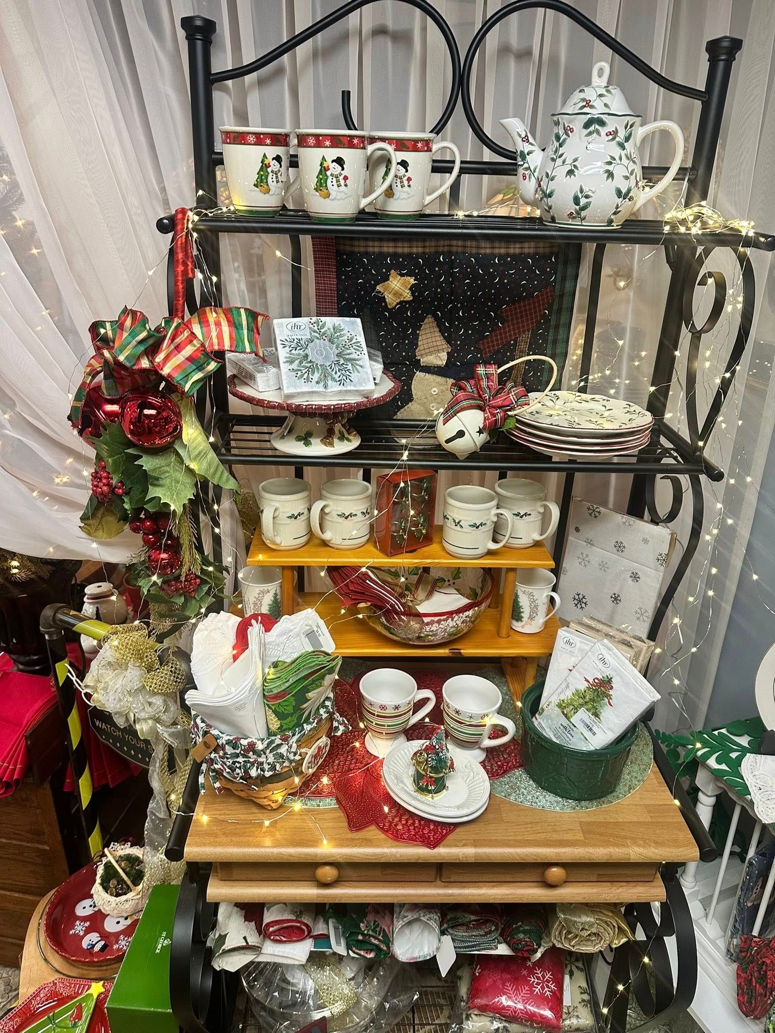 Christmas-themed tea set display on a black metal shelf, decorated with lights and festive ornaments.