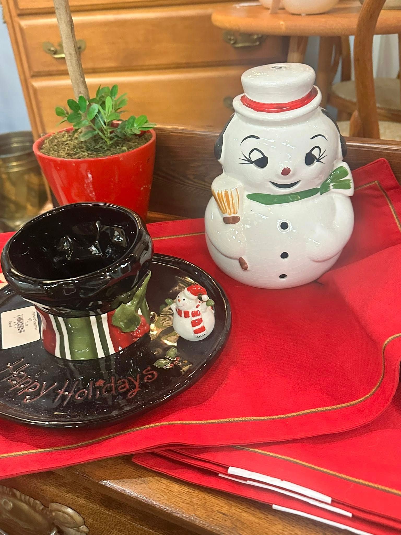 Snowman figurine and holiday-themed cup and saucer set on red cloth.