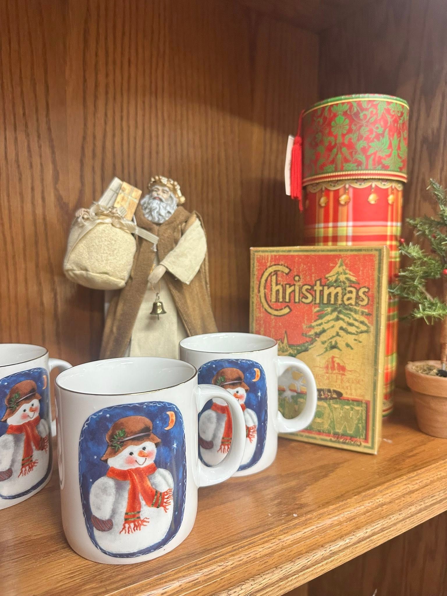 Shelf with Christmas mugs, Santa figure, festive boxes, and a Christmas sign.