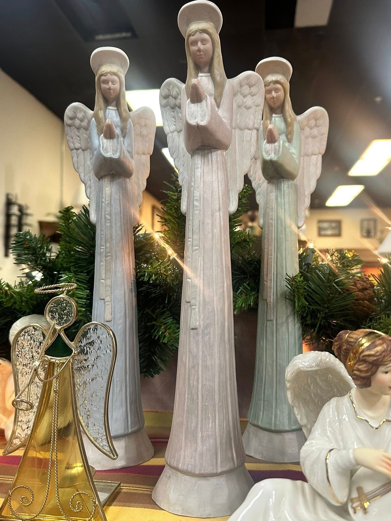 Three tall angel figurines with wings, holding boxes, and a few other angel decorations in a display.