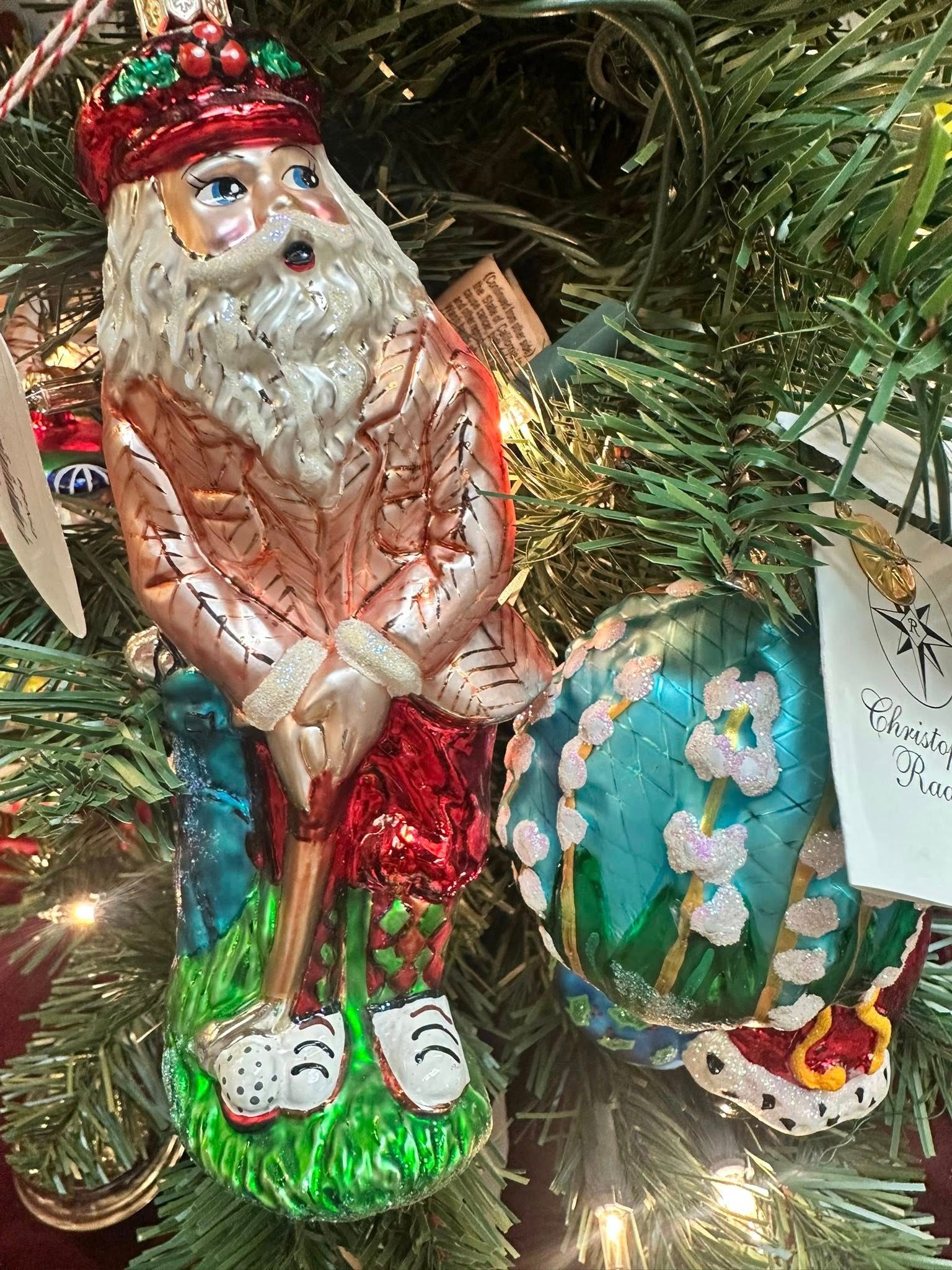 Ornament of Santa Claus playing golf on a Christmas tree. Santa wears golf attire and has a surprised expression.