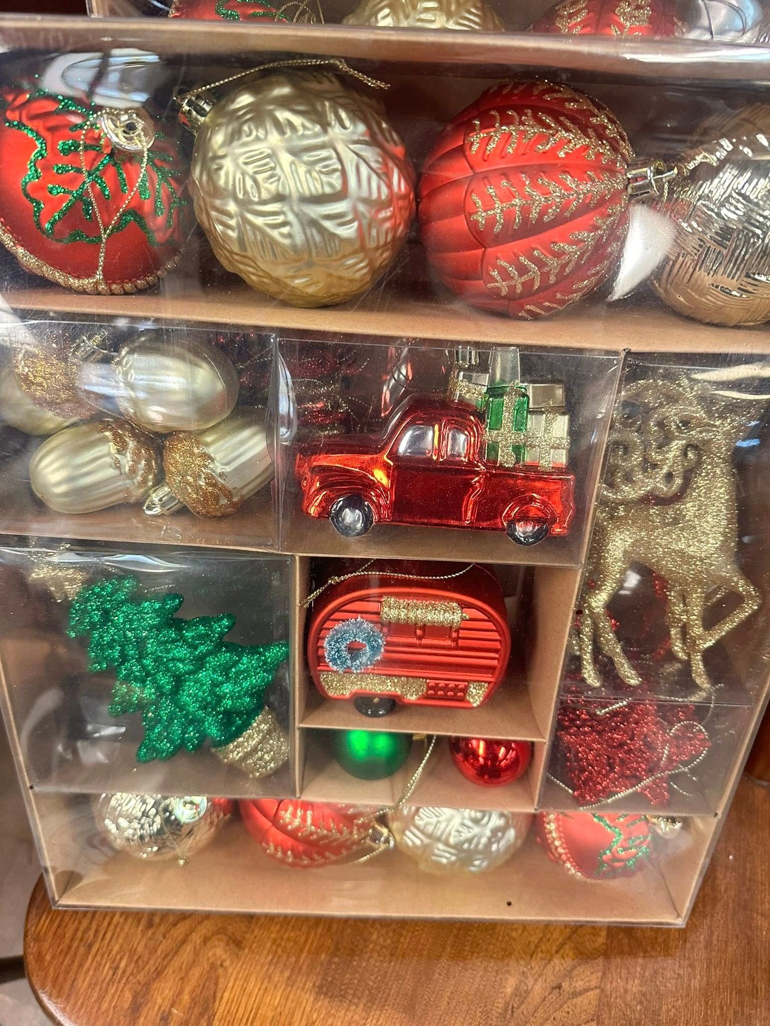 Christmas ornament set in a clear box, featuring red, gold, and green decorations.
