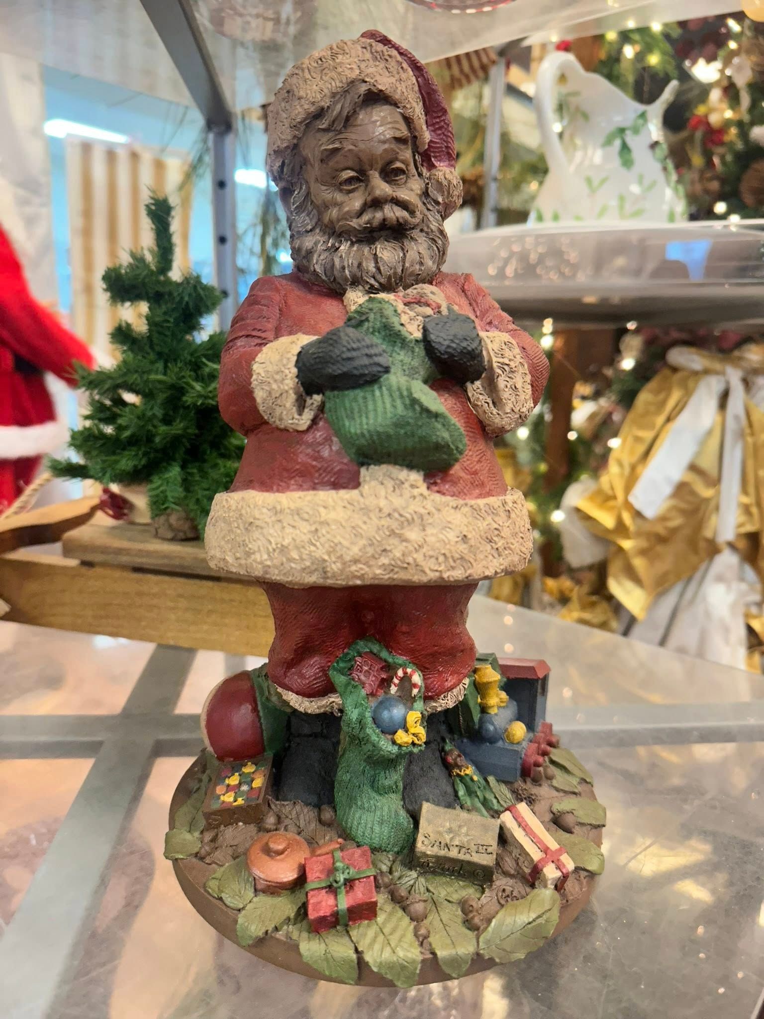 Santa Claus figurine in red suit and cap holding a green stocking.