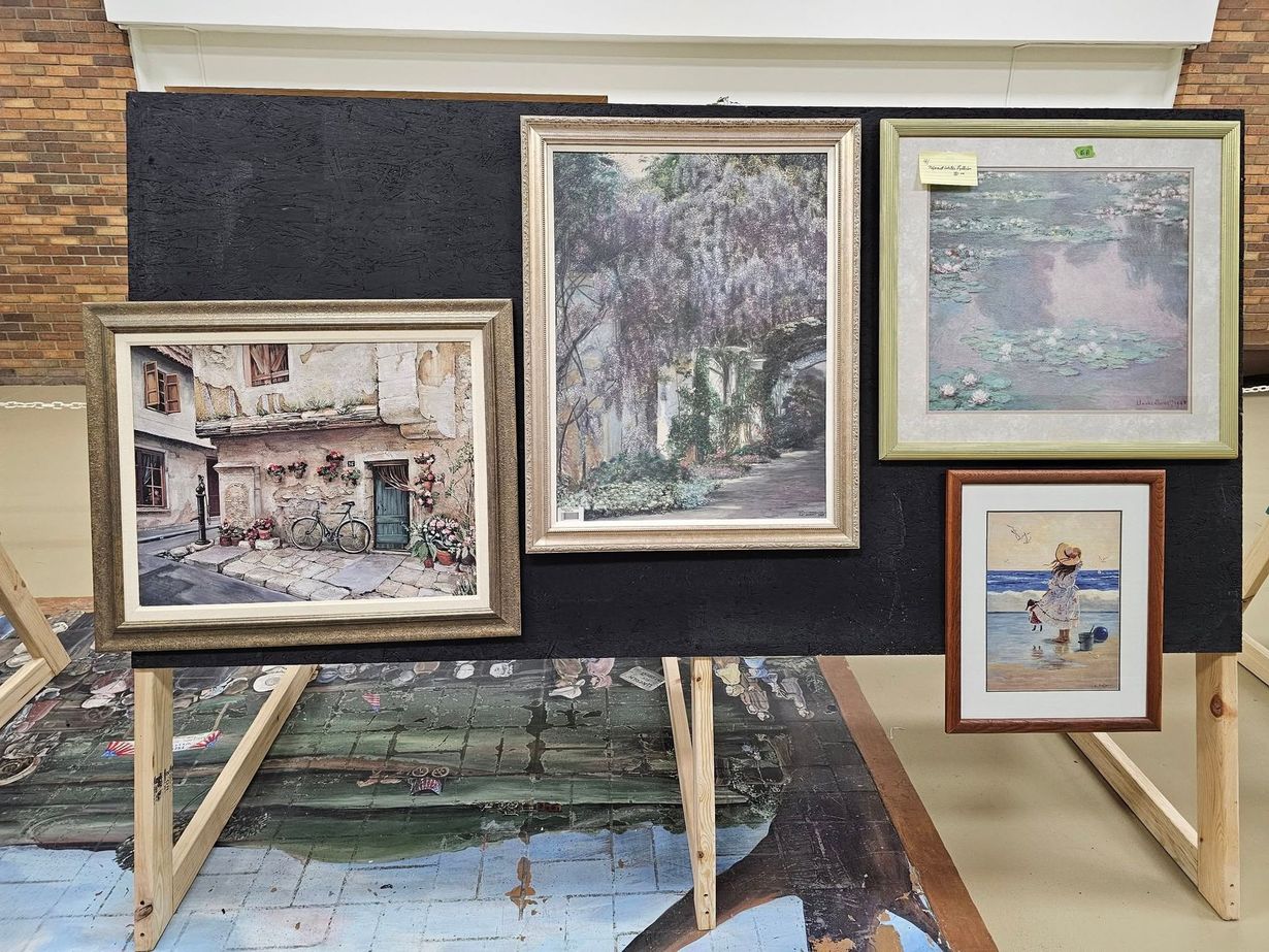 Paintings of various landscapes and buildings displayed on a black board and easel.