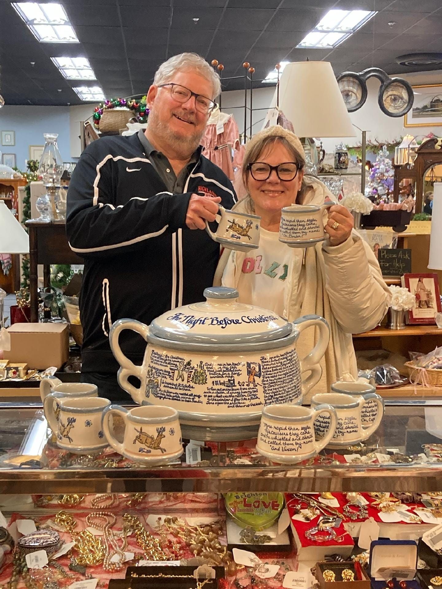 Couple holding teacups with large teapot. They smile in an antique shop, surrounded by pottery.