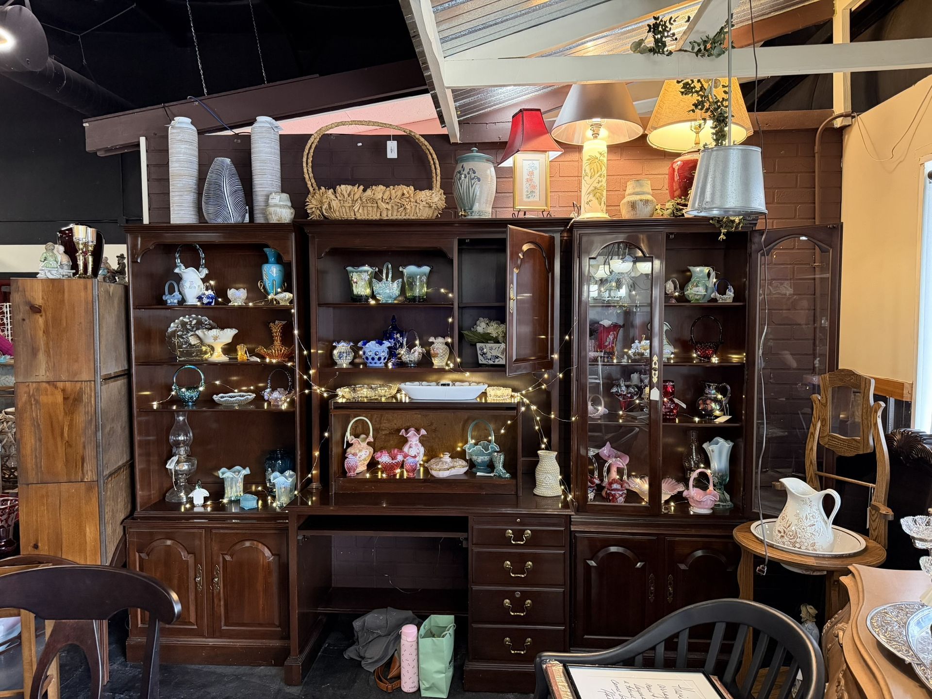 Antique wooden display cabinet filled with glassware and ceramics in a vintage shop interior
