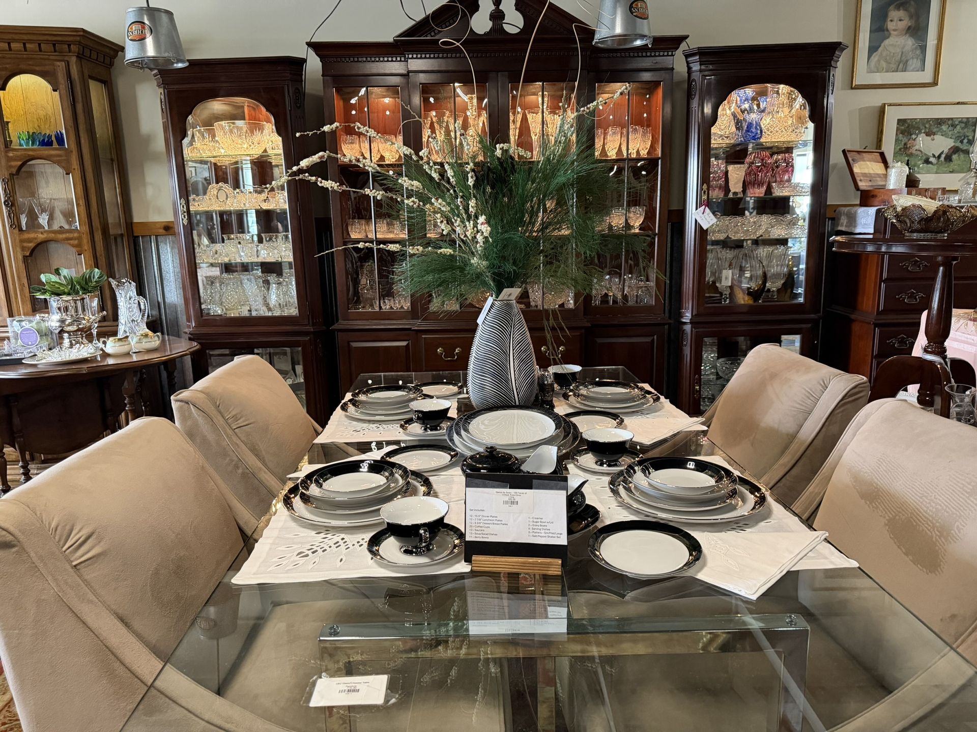 Elegant dining room with a glass table set for a formal meal and a dark wood china cabinet in the background