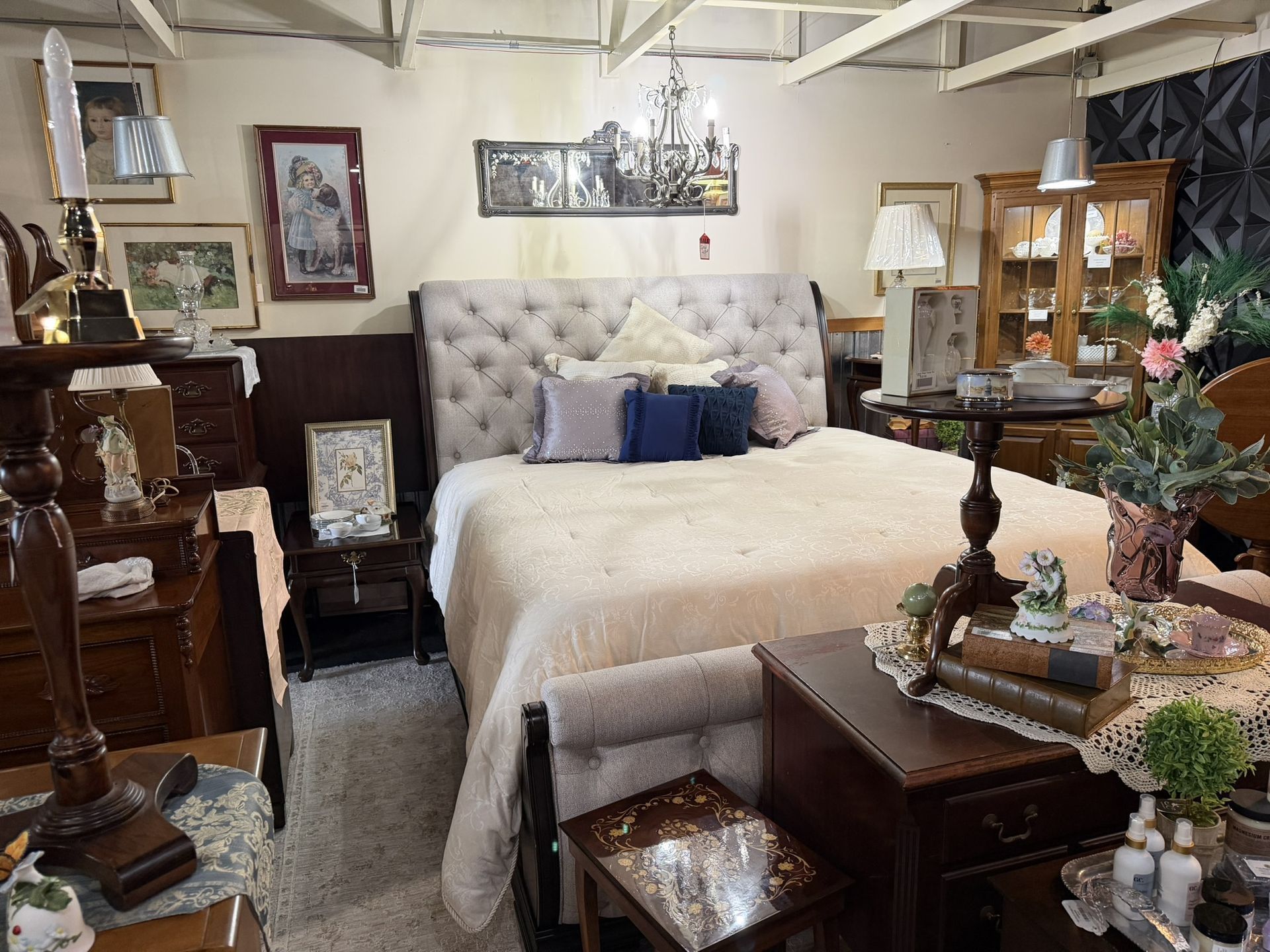 Cozy bedroom display with a tufted bed, dark wood furniture, lamp, and floral decor