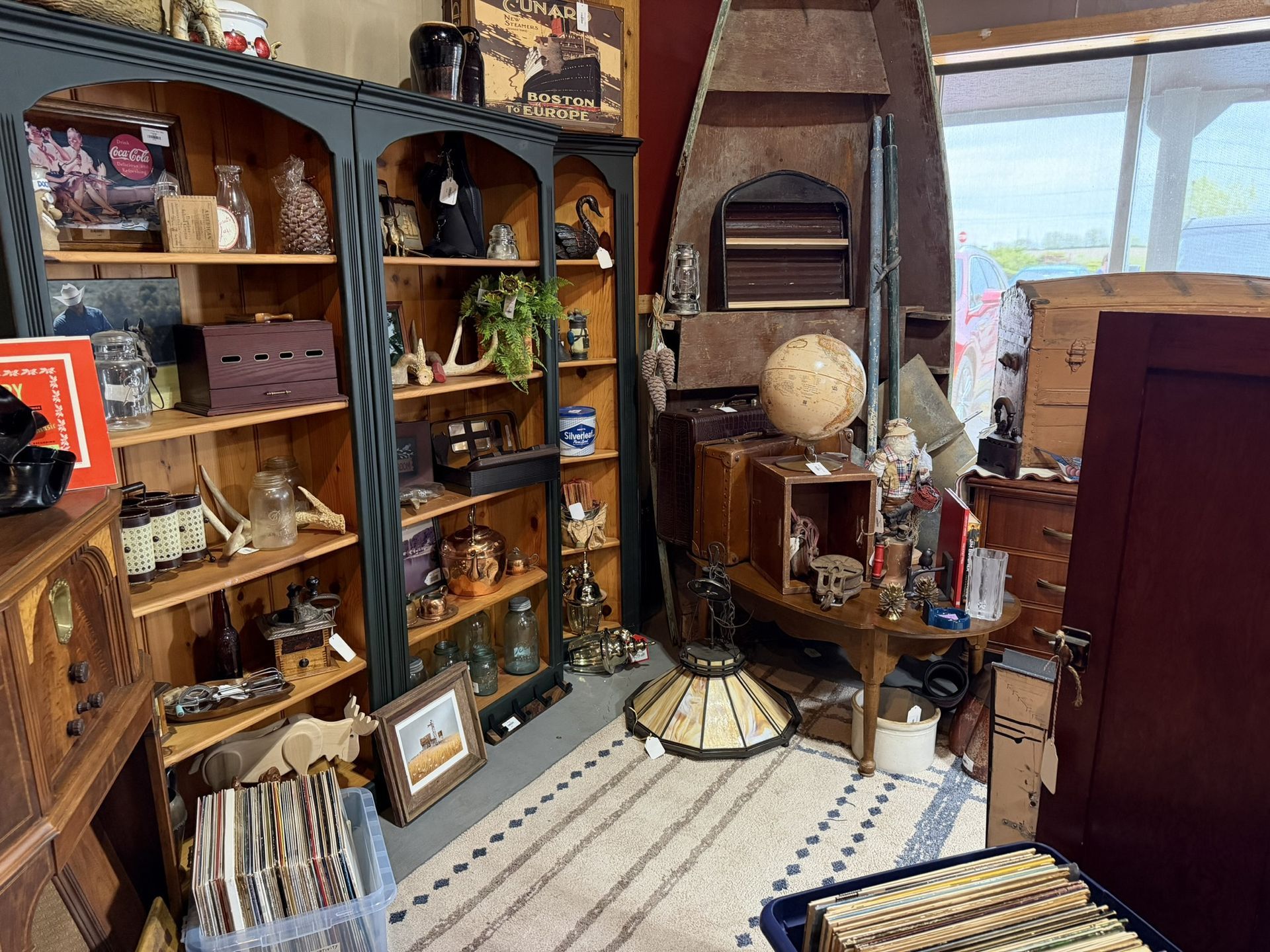 Cluttered antique shop interior with wooden shelves, vintage decor, globe, rug, and daylight from a window