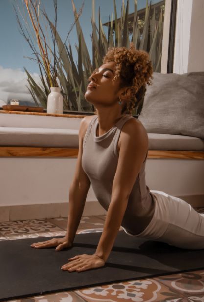 Woman in yoga pose on mat, eyes closed, with sunlight streaming through window.