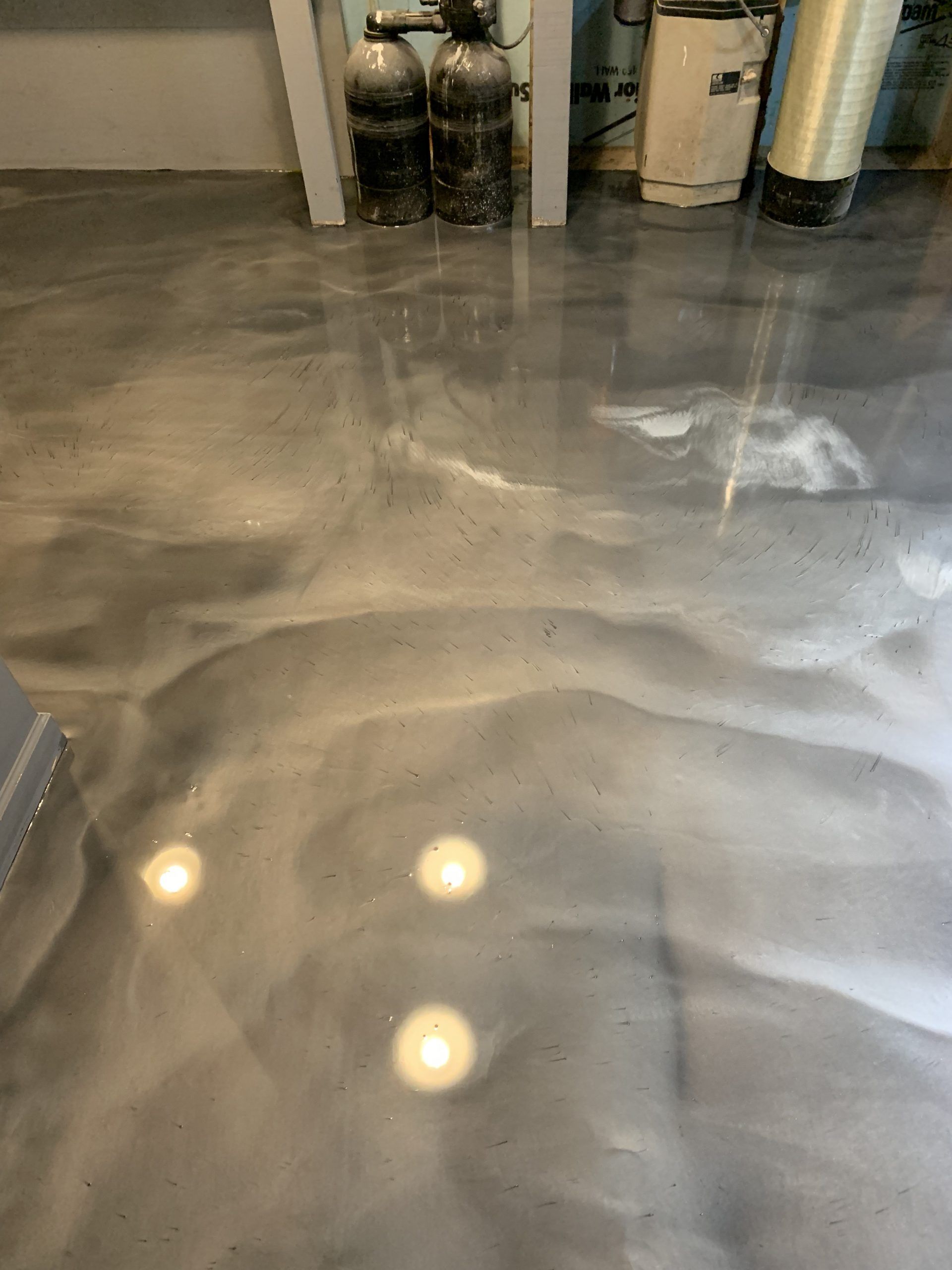 Shiny wet concrete floor in a garage with reflections of overhead lights and storage items along the wall