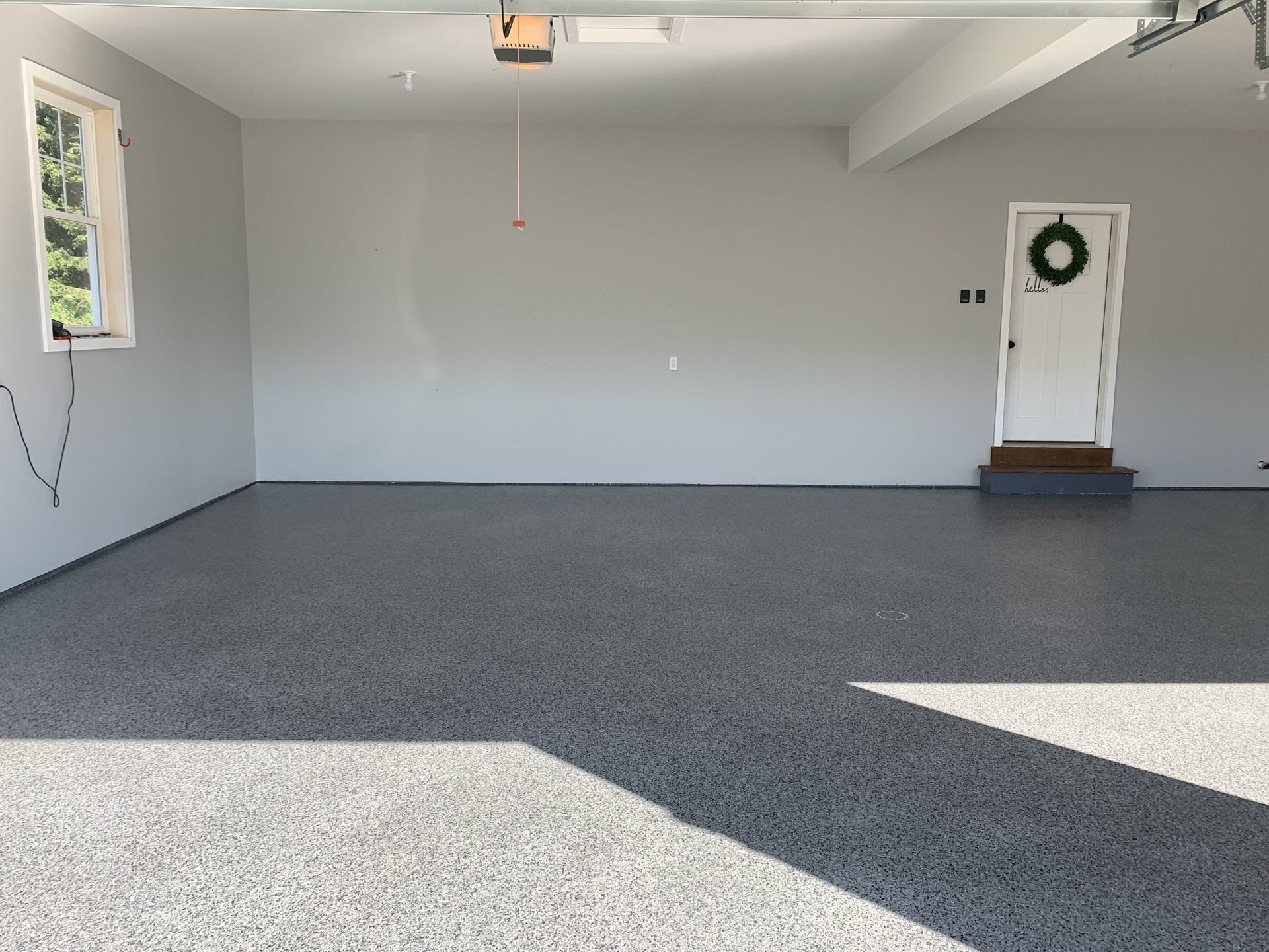 Empty garage interior with gray carpeted floor, white walls, and a small wreath on the far wall.