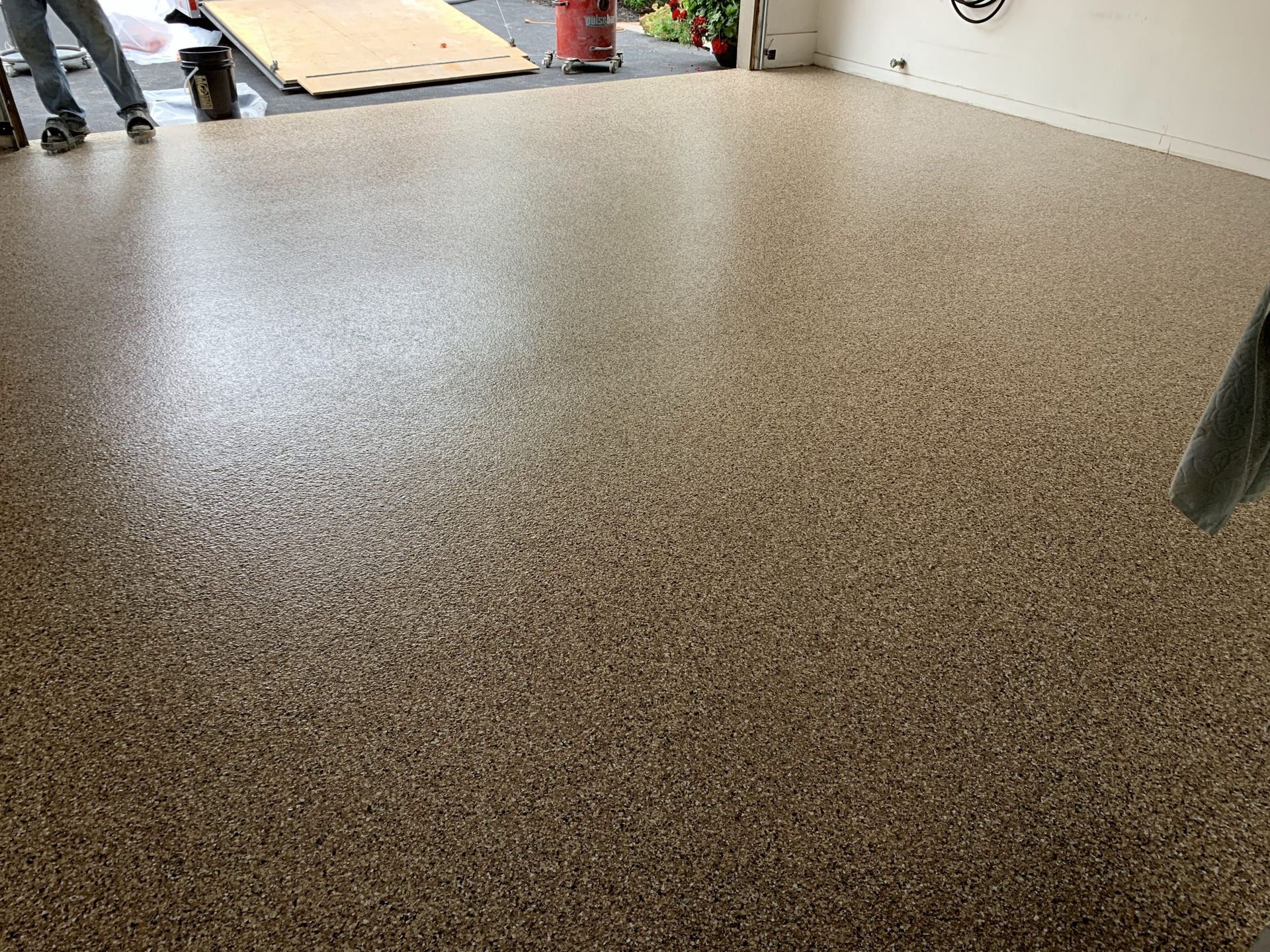 Speckled epoxy floor being installed in a garage, with workers visible near the doorway