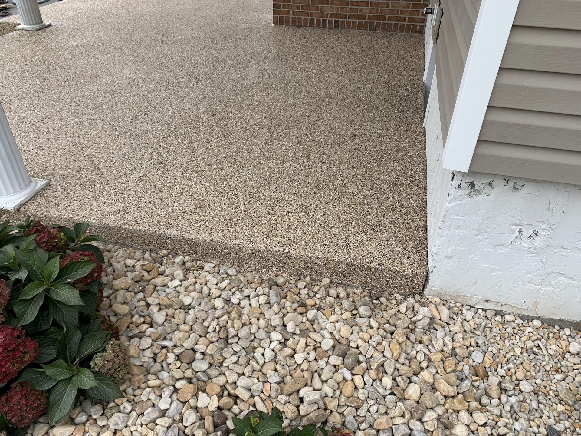 Front porch with textured concrete step, pebble ground cover, white railing, and house siding.