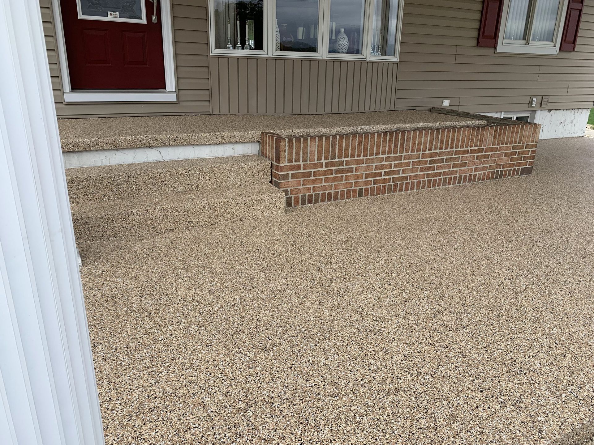 Gravel yard with a brick planter beneath beige house siding and a red front door