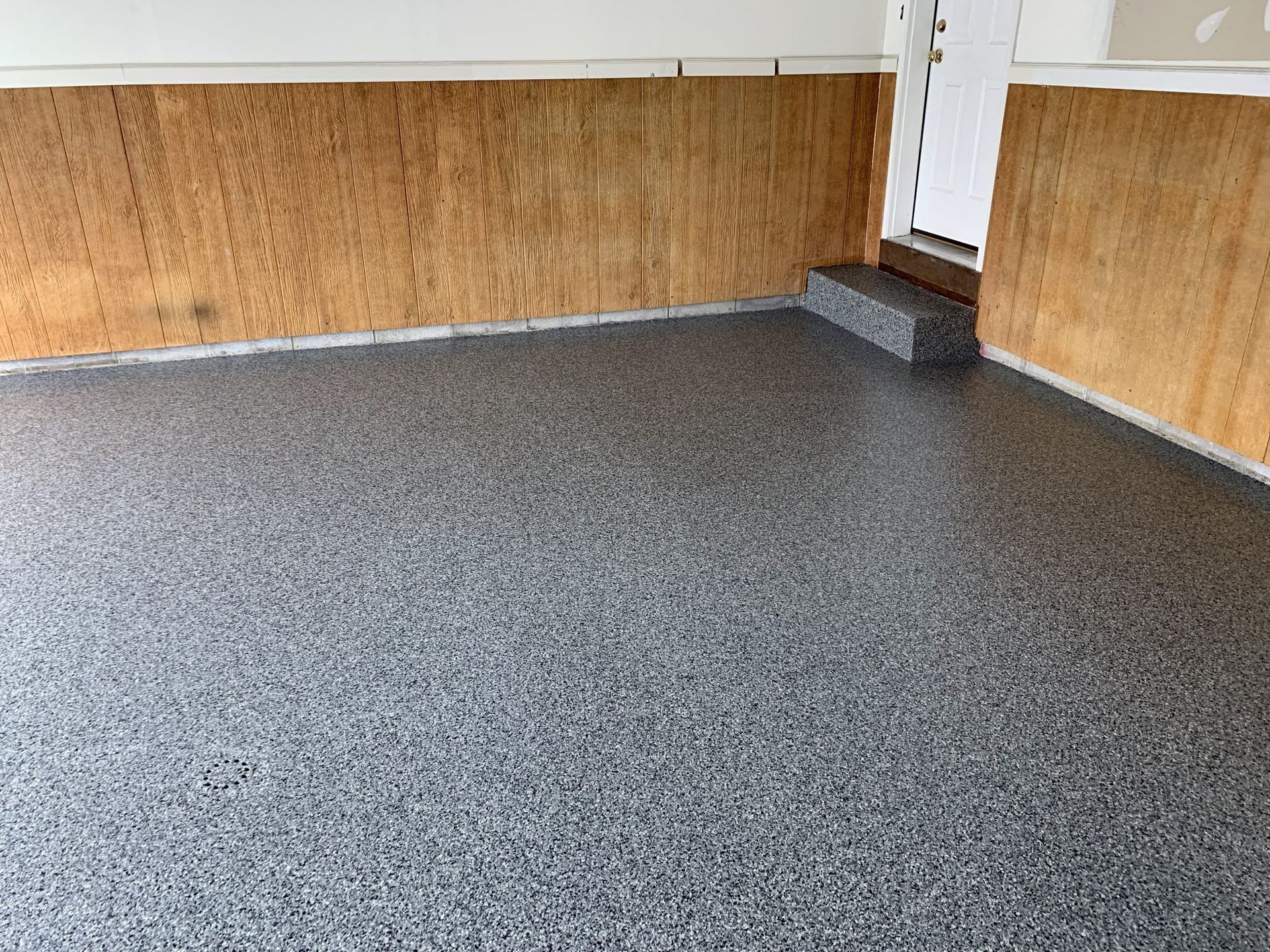 Empty room with speckled gray floor, wood-paneled walls, and a small corner step.