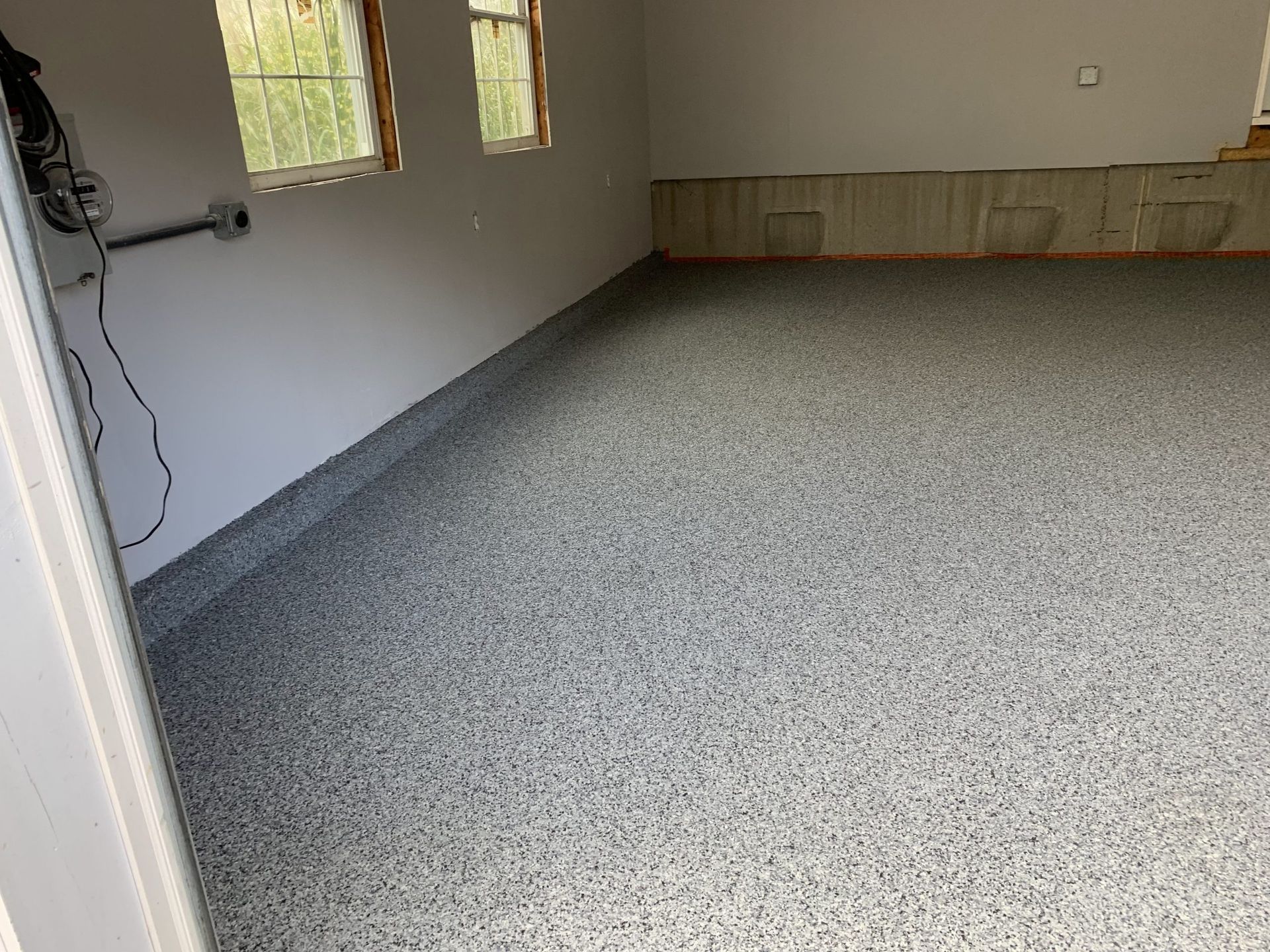 Empty carpeted room with gray walls, two windows, and a wall-mounted fan on the left.