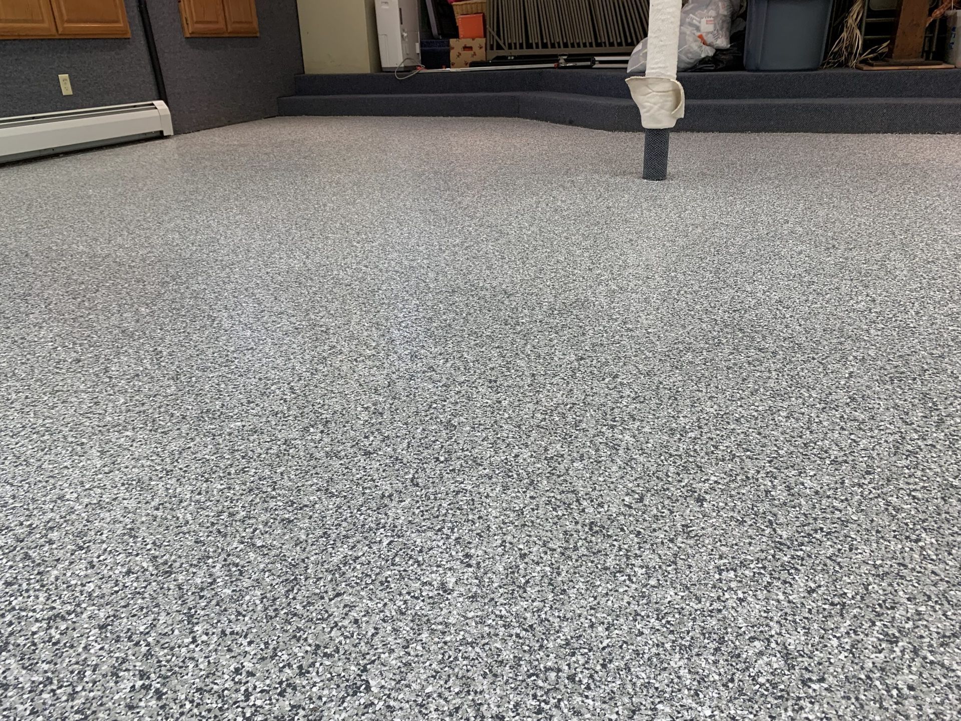 Speckled gray floor in a room, with furniture visible along the back wall.