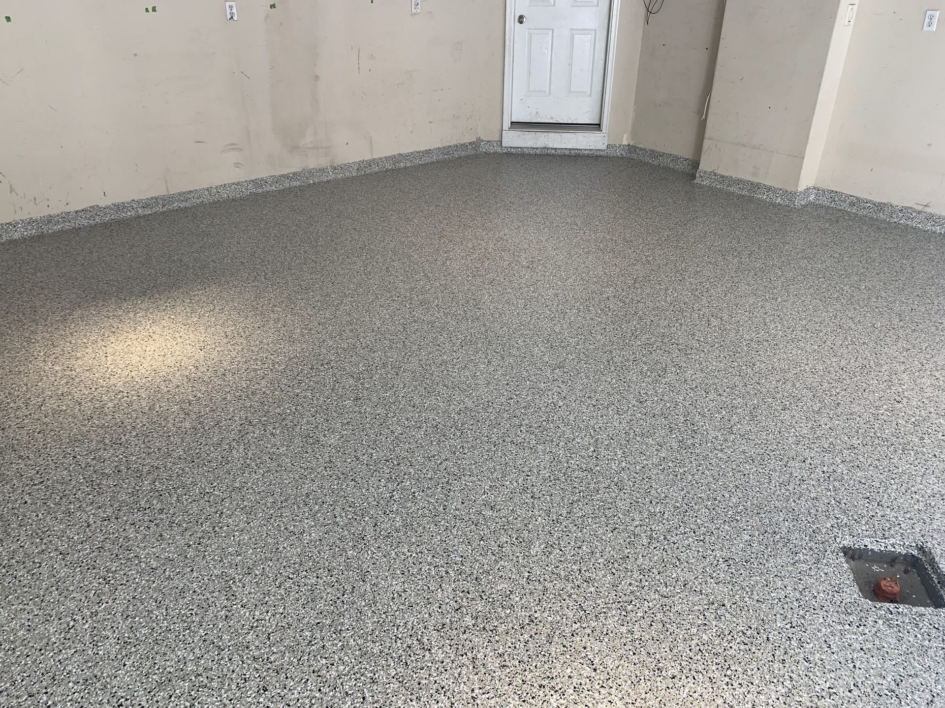 Empty speckled garage floor with a white door and a floor drain