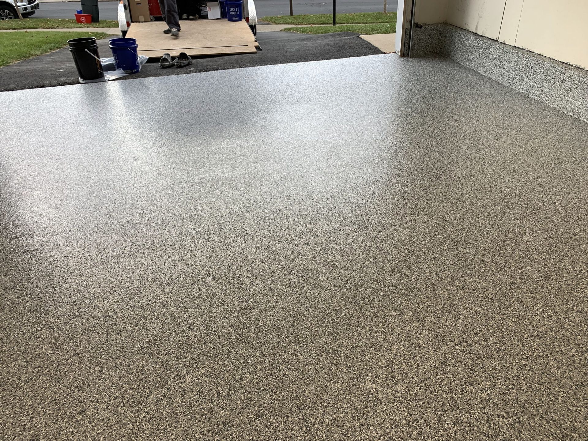 Speckled epoxy floor in a garage opening to a driveway with buckets and tools in the background