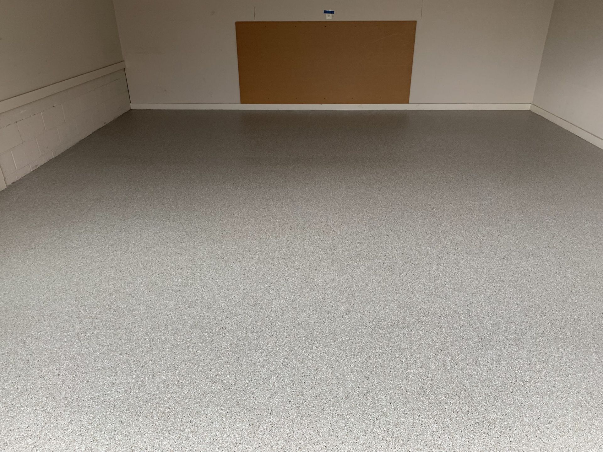 Empty gray carpeted room with white walls and a brown bulletin board on the far wall