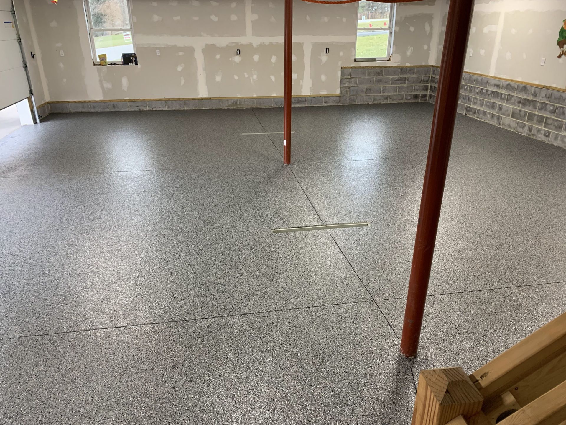 Empty unfinished basement with gray speckled floor, exposed walls, and support posts