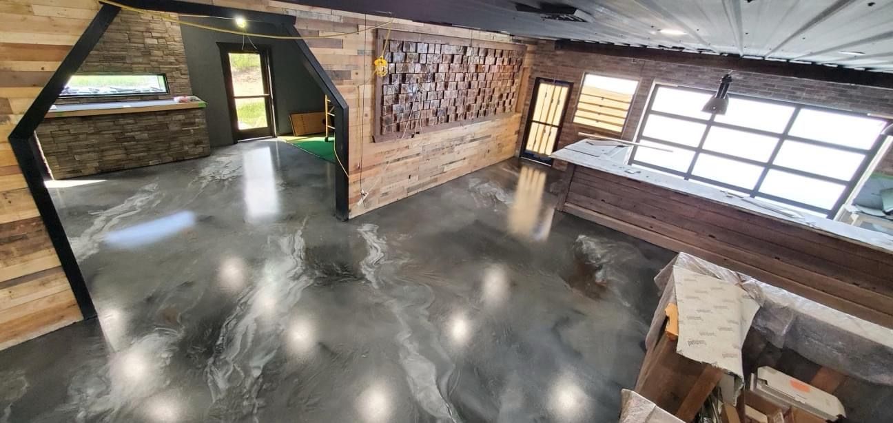 Loft-style room with polished concrete floor, exposed brick walls, large windows, and a staircase