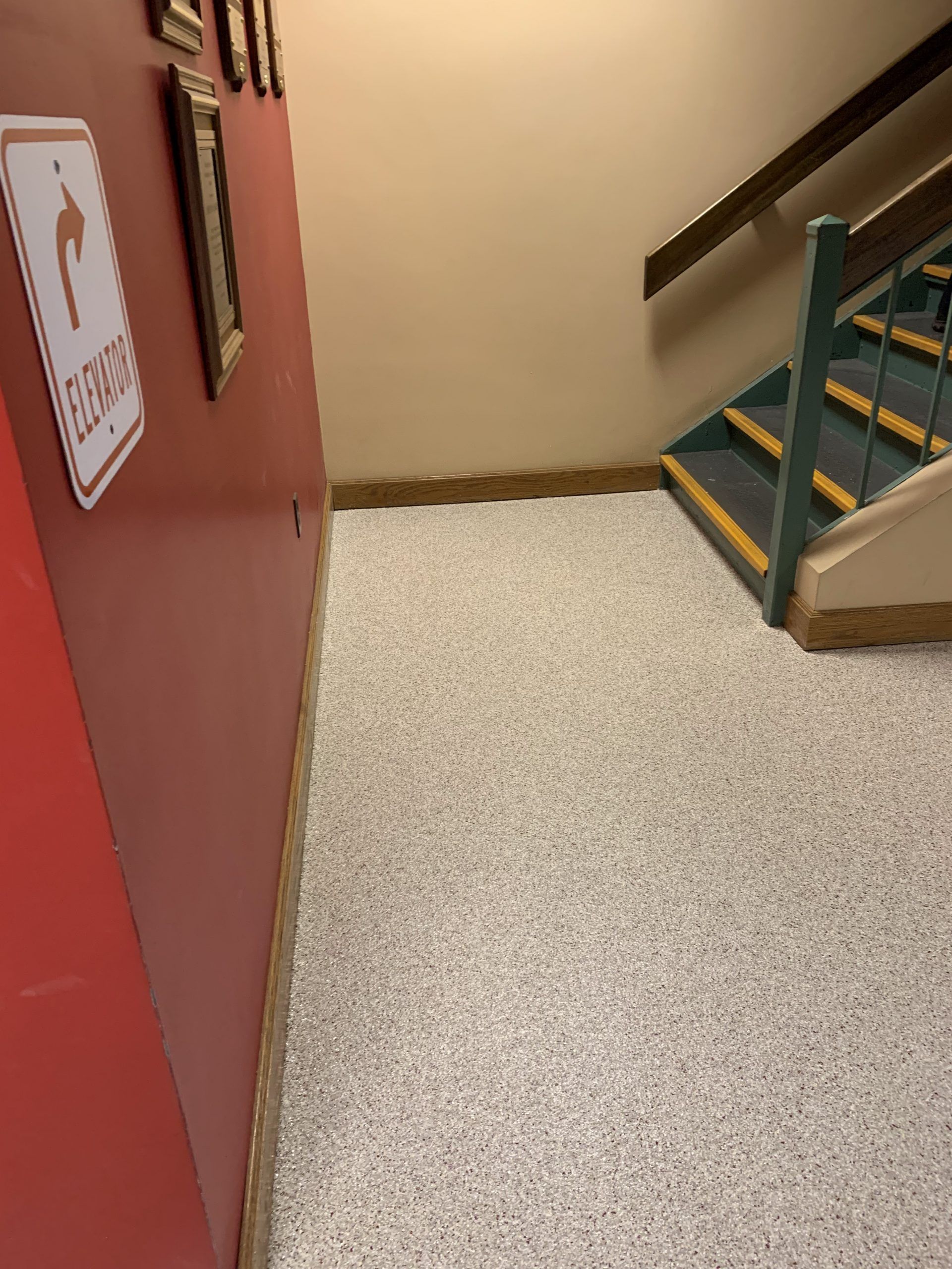 Indoor stairwell with a red wall, beige speckled floor, and green-railed stairs