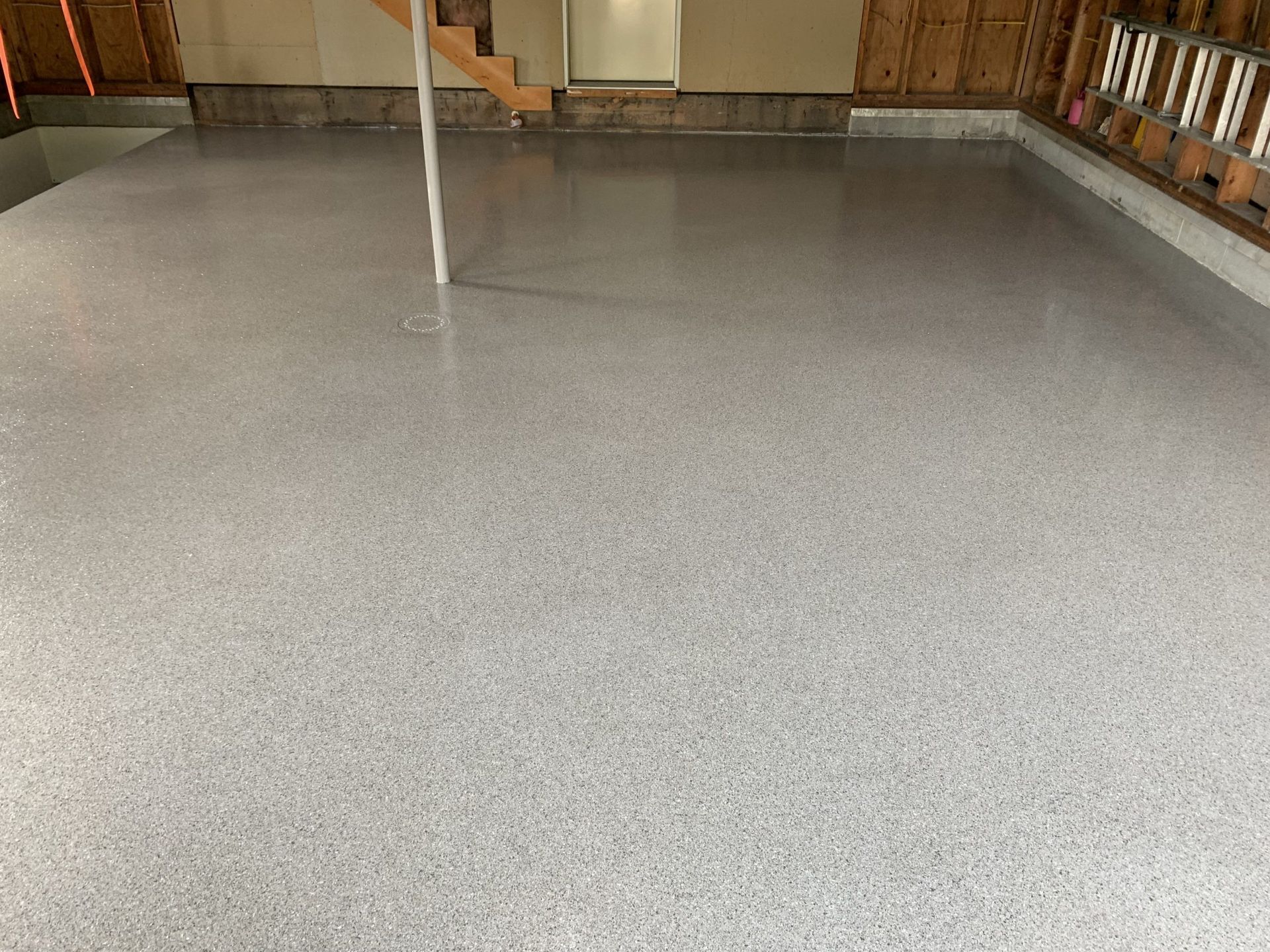 Empty gray speckled floor in a garage or workshop with wooden walls and a pole at center.