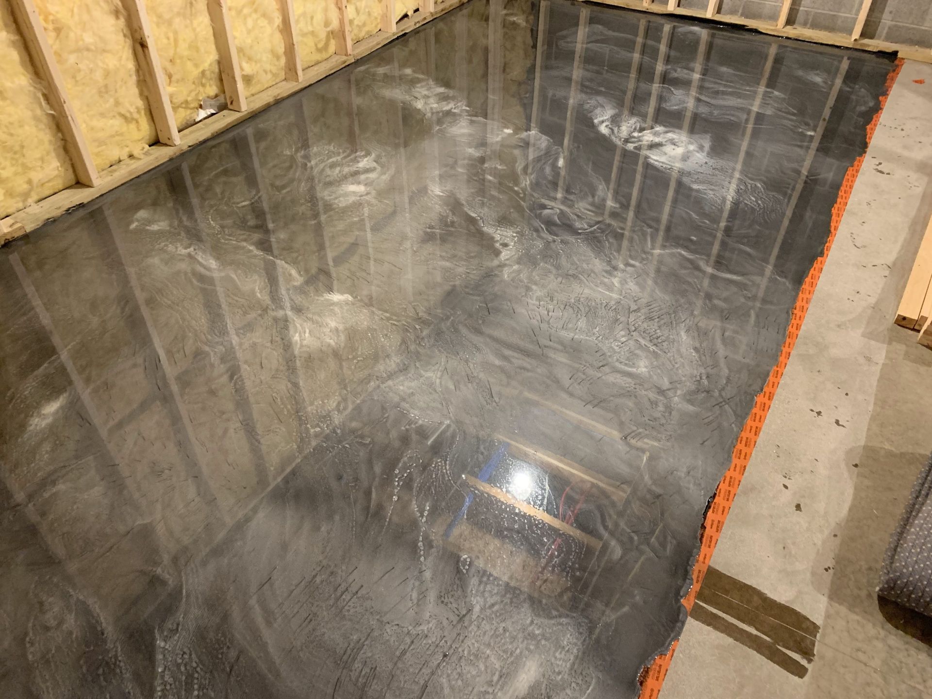 Reflective black waterproof membrane installed on a floor in a framed room under construction