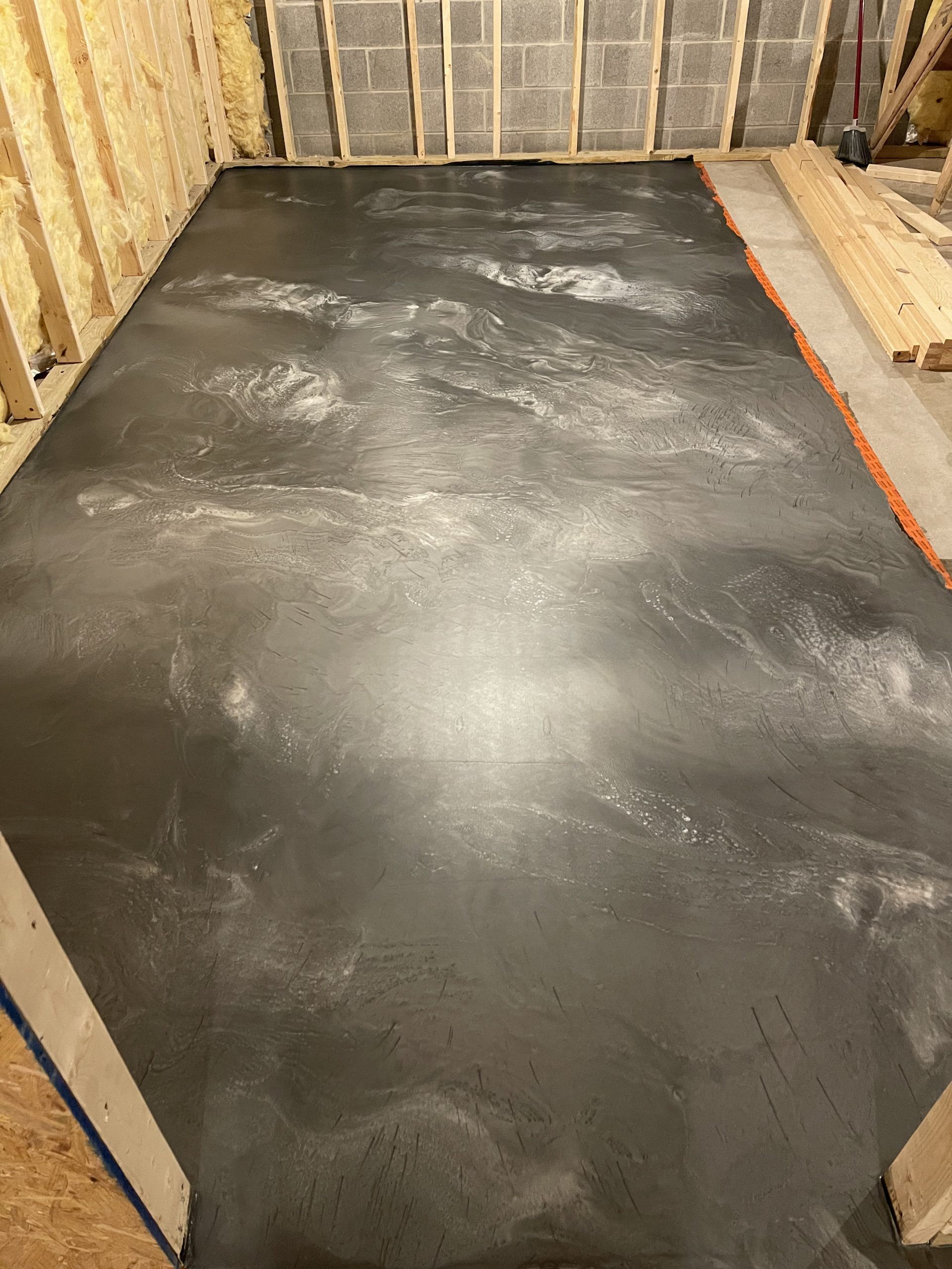 Unfinished basement floor with fresh black concrete and exposed wall framing around the edges