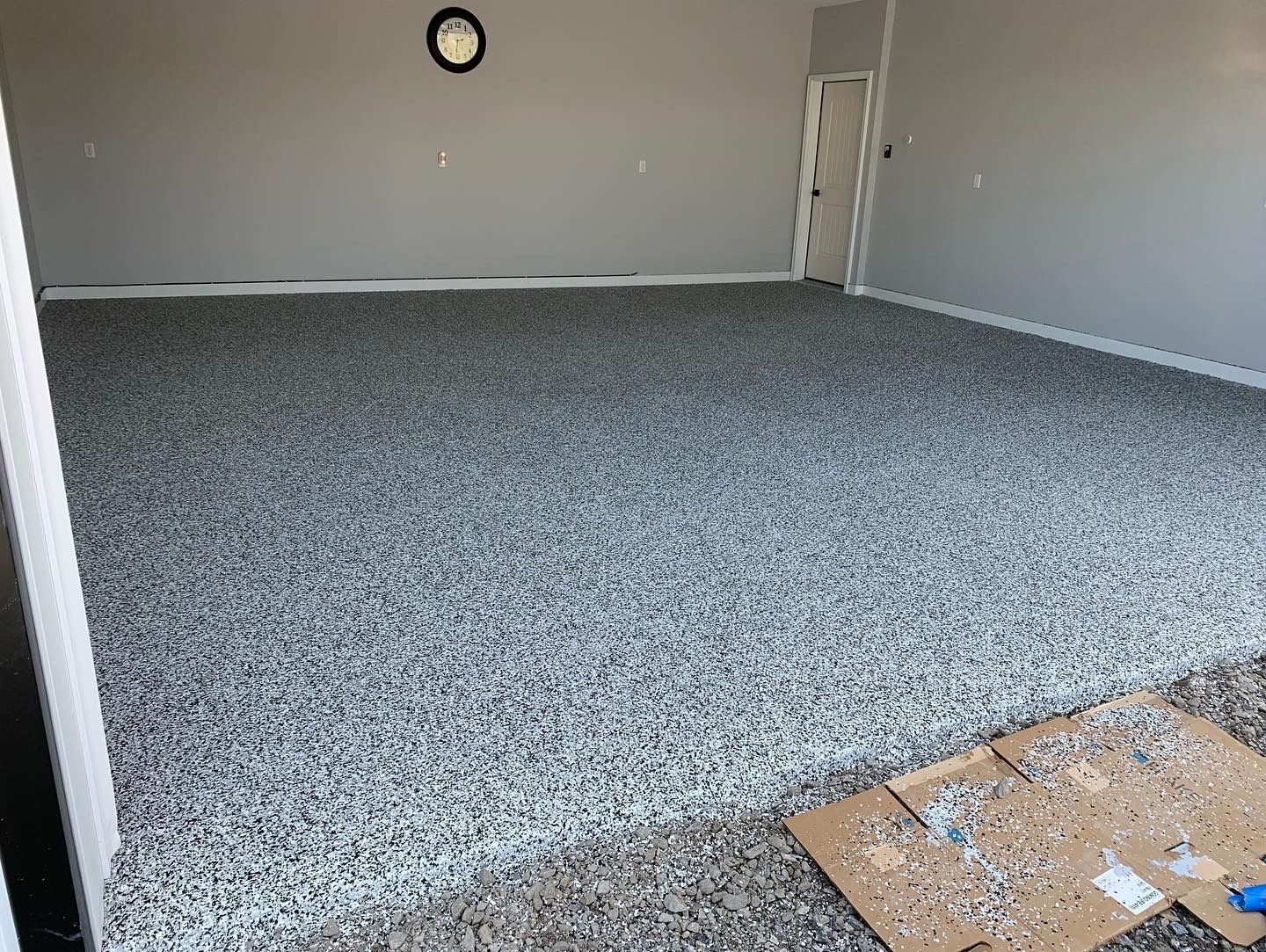 Empty carpeted room with gray walls and a white door, viewed from the corner.